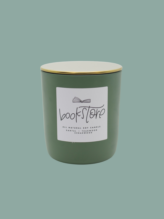 A matte green glass candle jar with a gold lid, labeled 'Bookstore'.