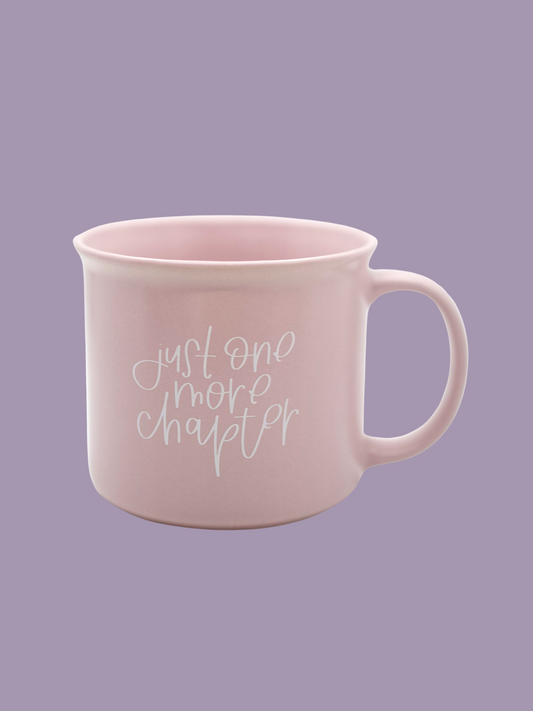 A matte lilac ceramic mug with the phrase 'Just One More Chapter' printed in white on the side, held against a purple background.