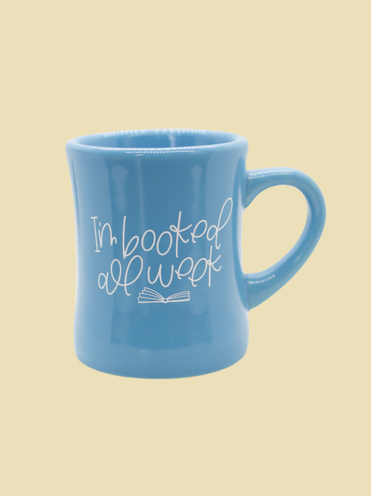 A blue ceramic mug with the text 'I'm booked all week' printed on it, featuring an open book graphic.