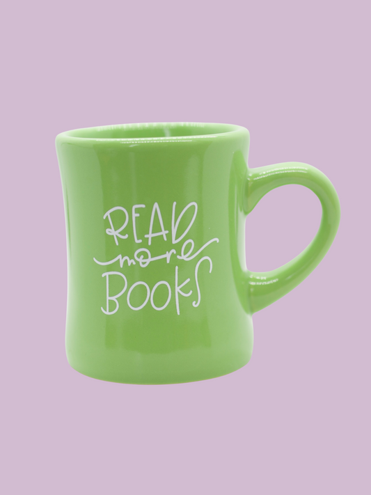 A green ceramic mug with the phrase 'READ more books' written in white hand-lettering on the side.