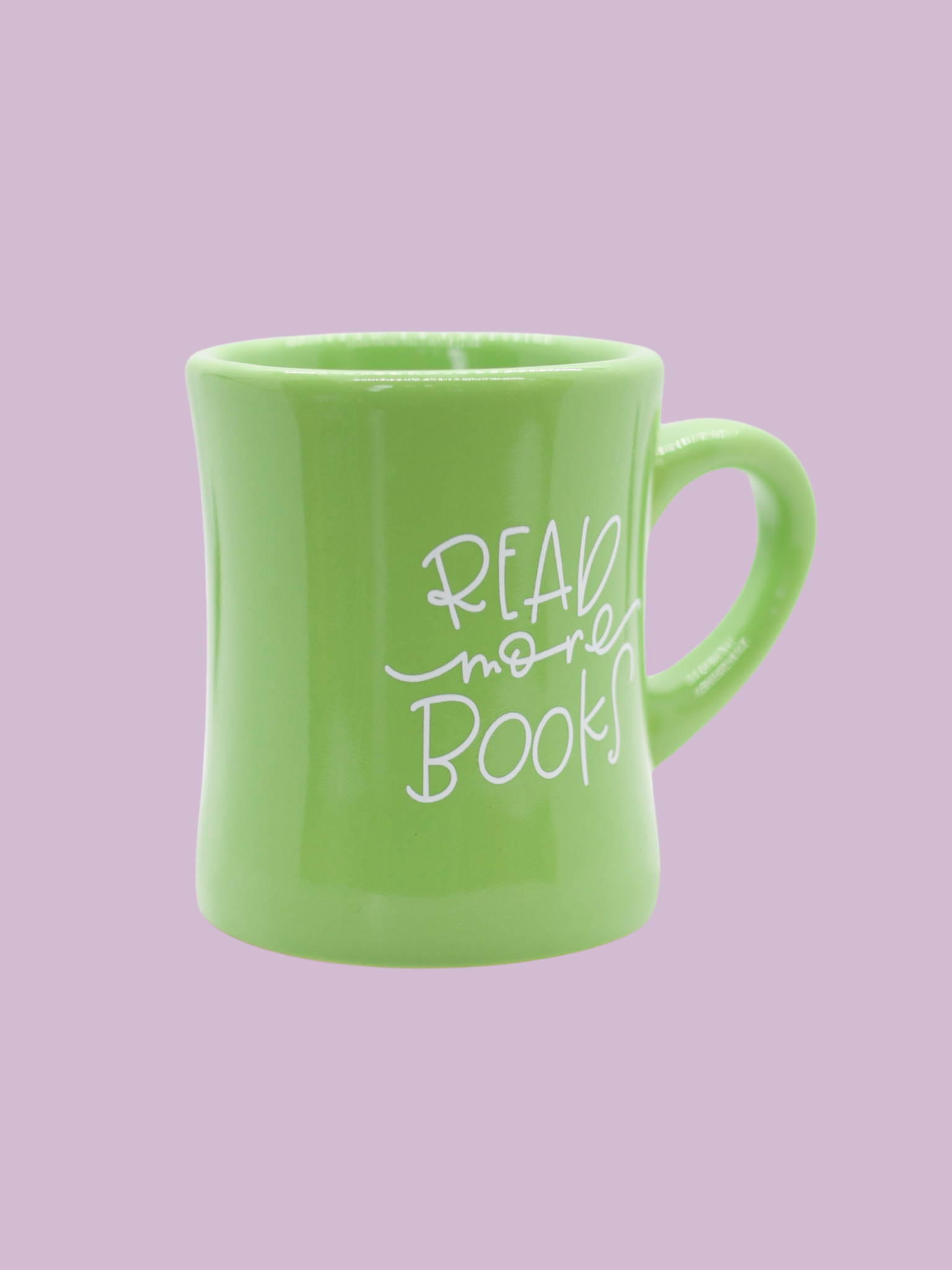 A green ceramic mug with the phrase 'READ more books' written in white hand-lettering on the side.