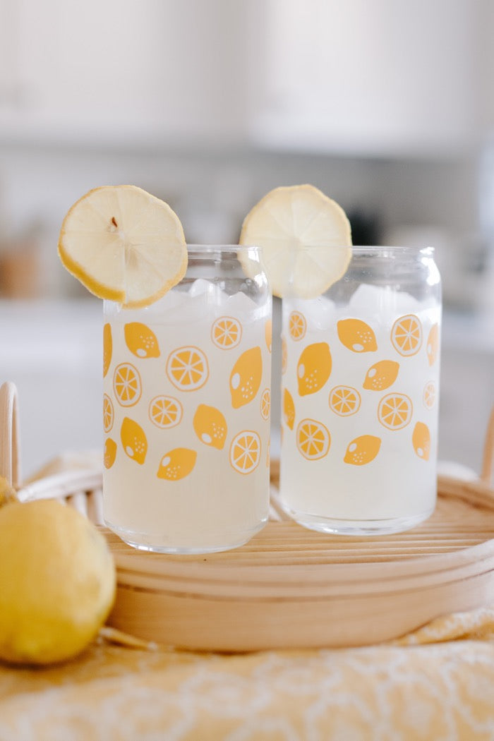 A clear can-shaped glass with lemon design wrapped around.