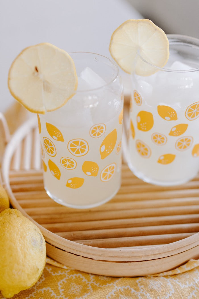 A clear can-shaped glass with lemon design wrapped around.