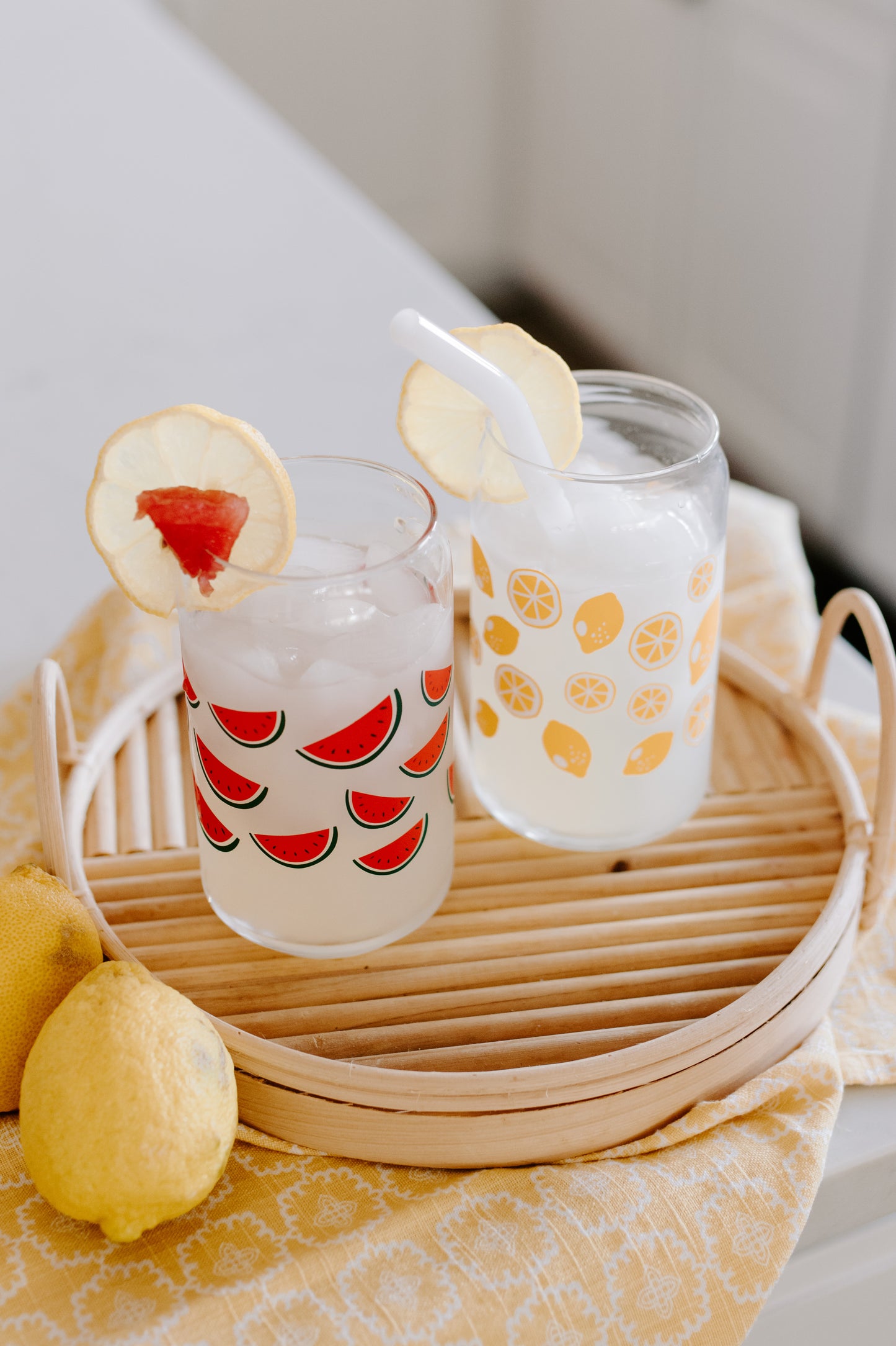 A pair of clear can-shaped glasses. One with lemon design and the other with watermelon design wrapped around.