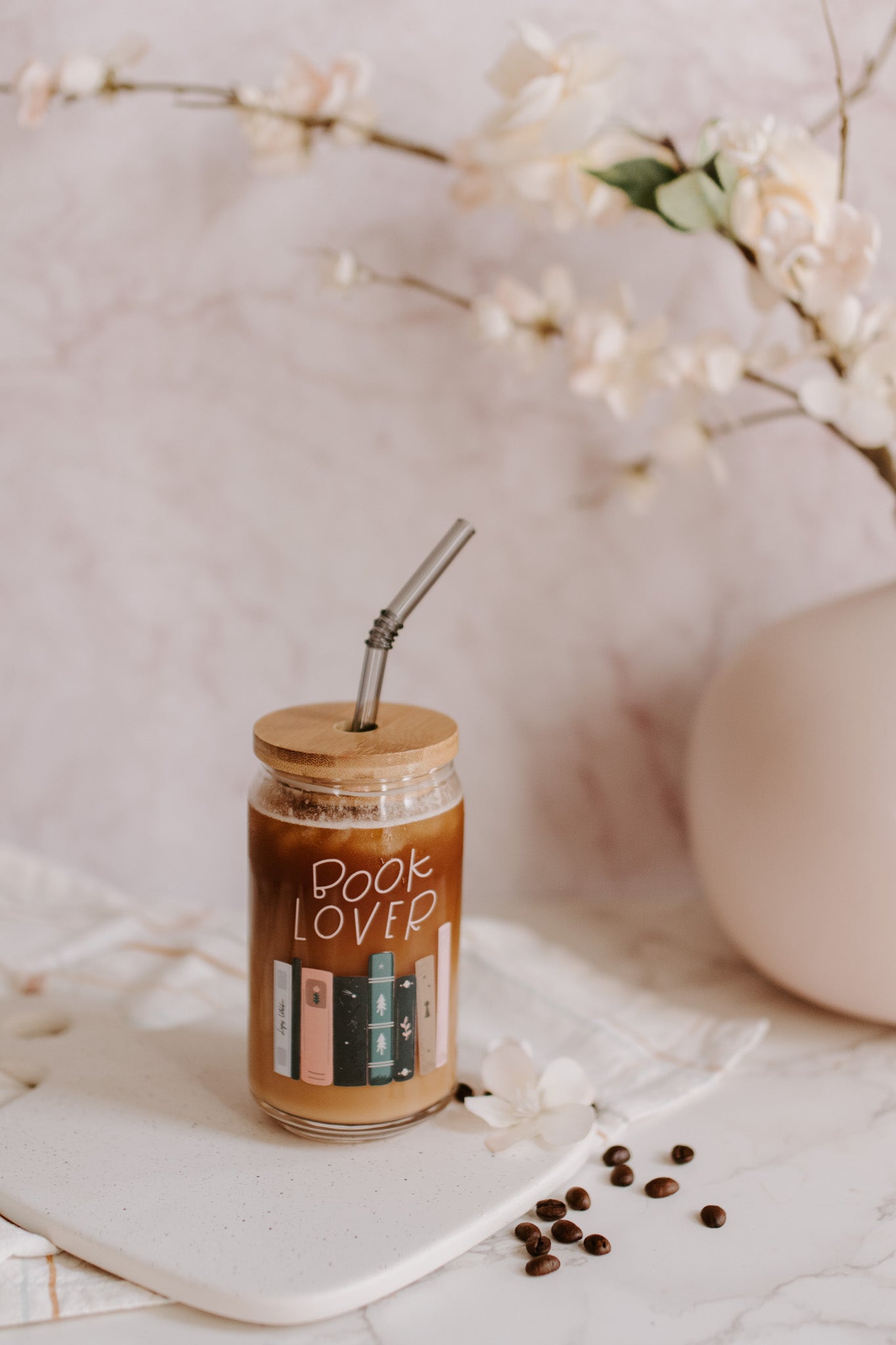 A clear glass can-shaped beverage holder with 'BOOK LOVER' text and a graphic of book spines on it.