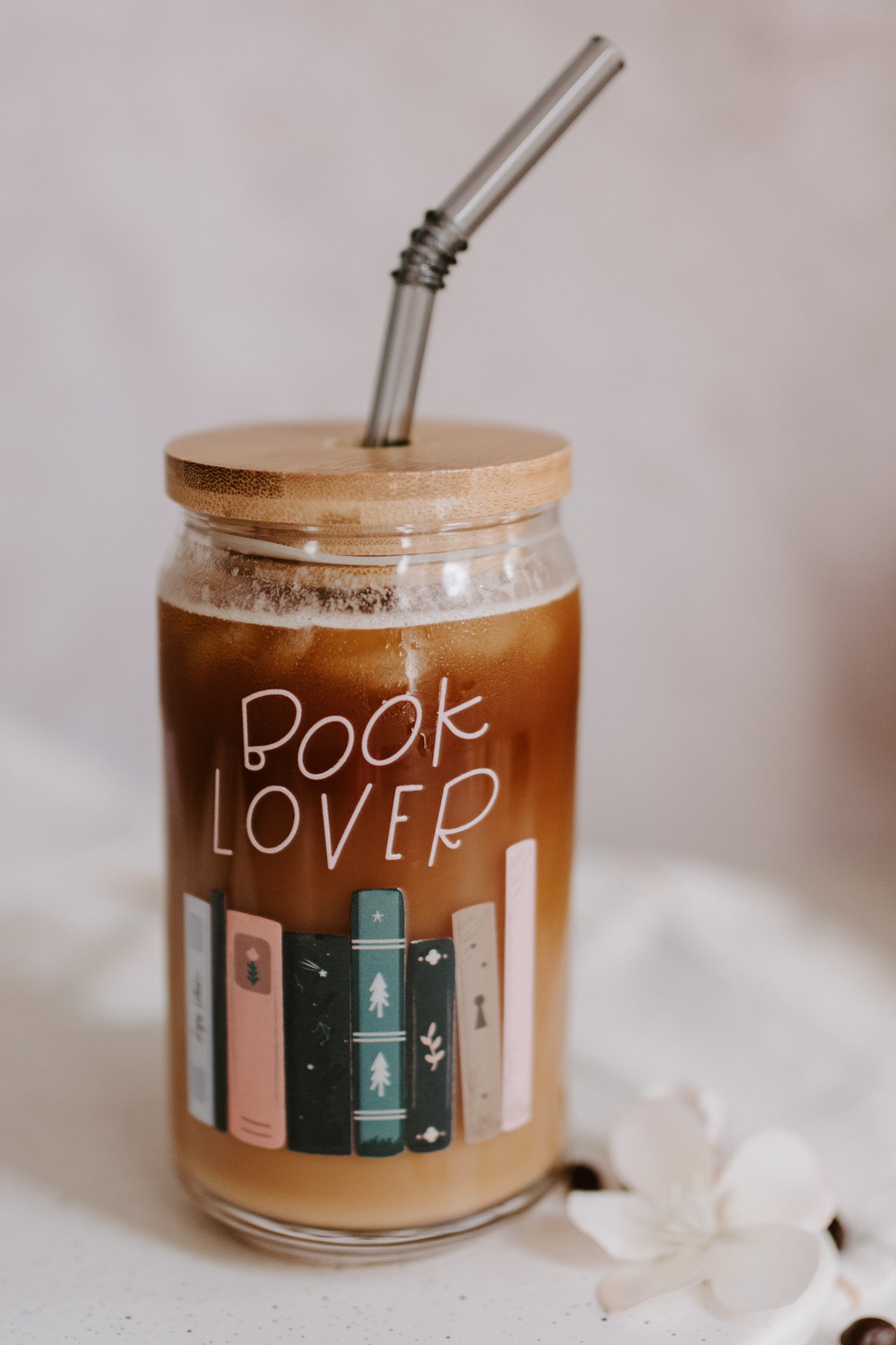 A clear glass can-shaped beverage holder with 'BOOK LOVER' text and a graphic of book spines on it.