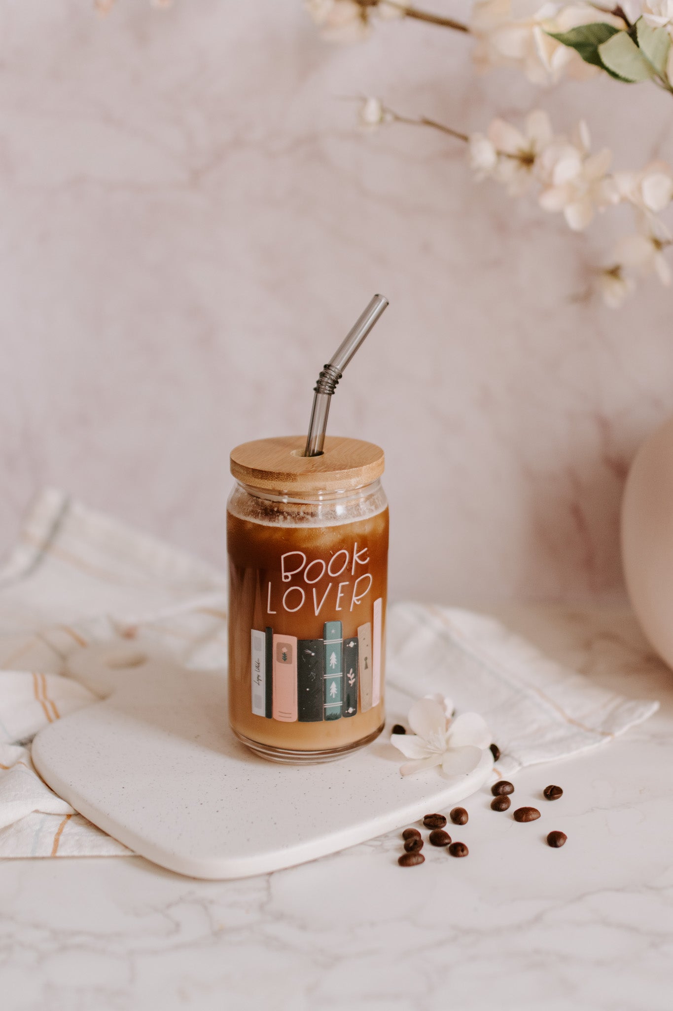 A clear glass can-shaped beverage holder with 'BOOK LOVER' text and a graphic of book spines on it.
