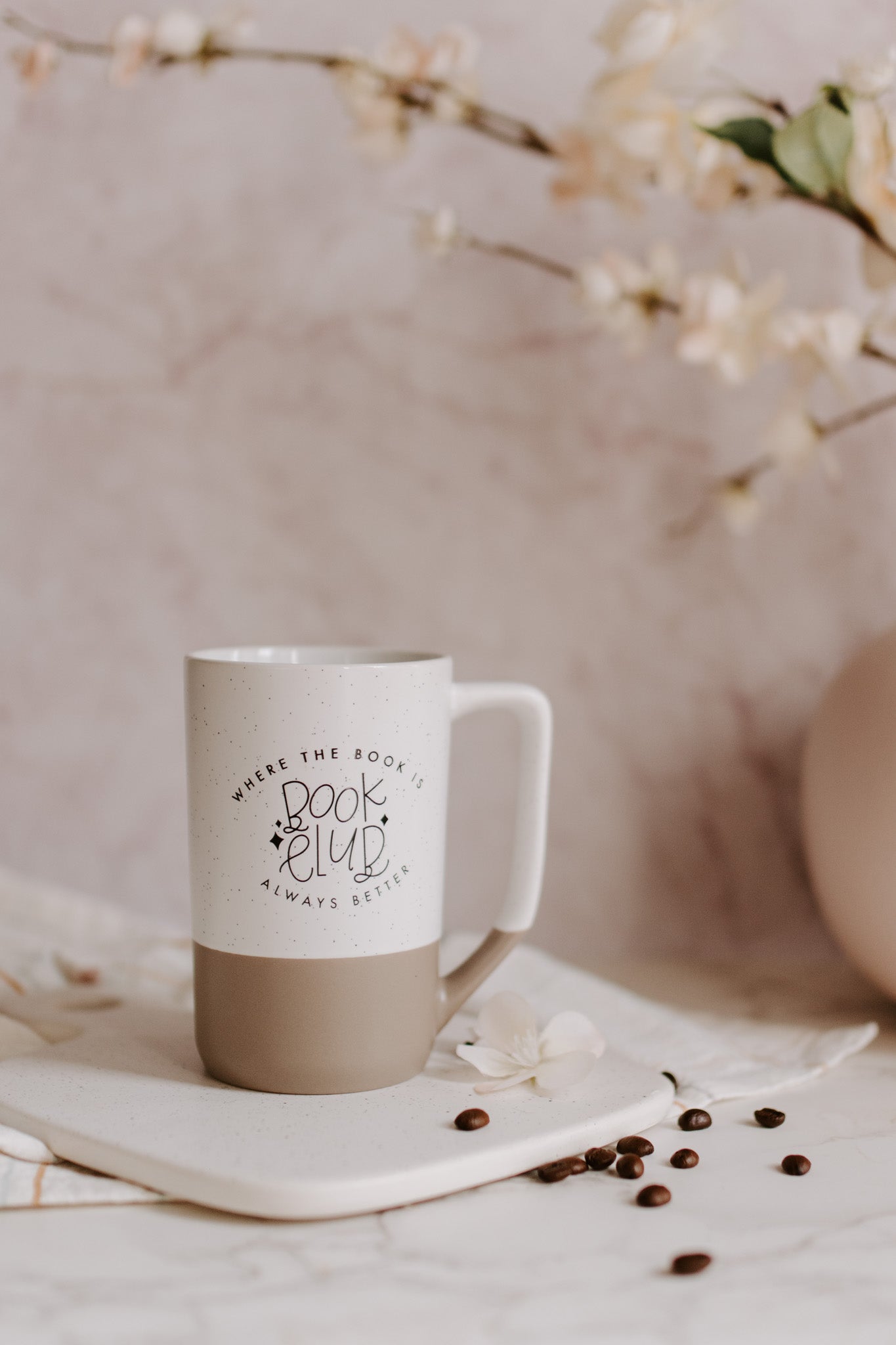 A two-tone ceramic mug with the upper part white with black speckles and the lower part taupe, featuring 'Book Club' text imprinted on the white part.