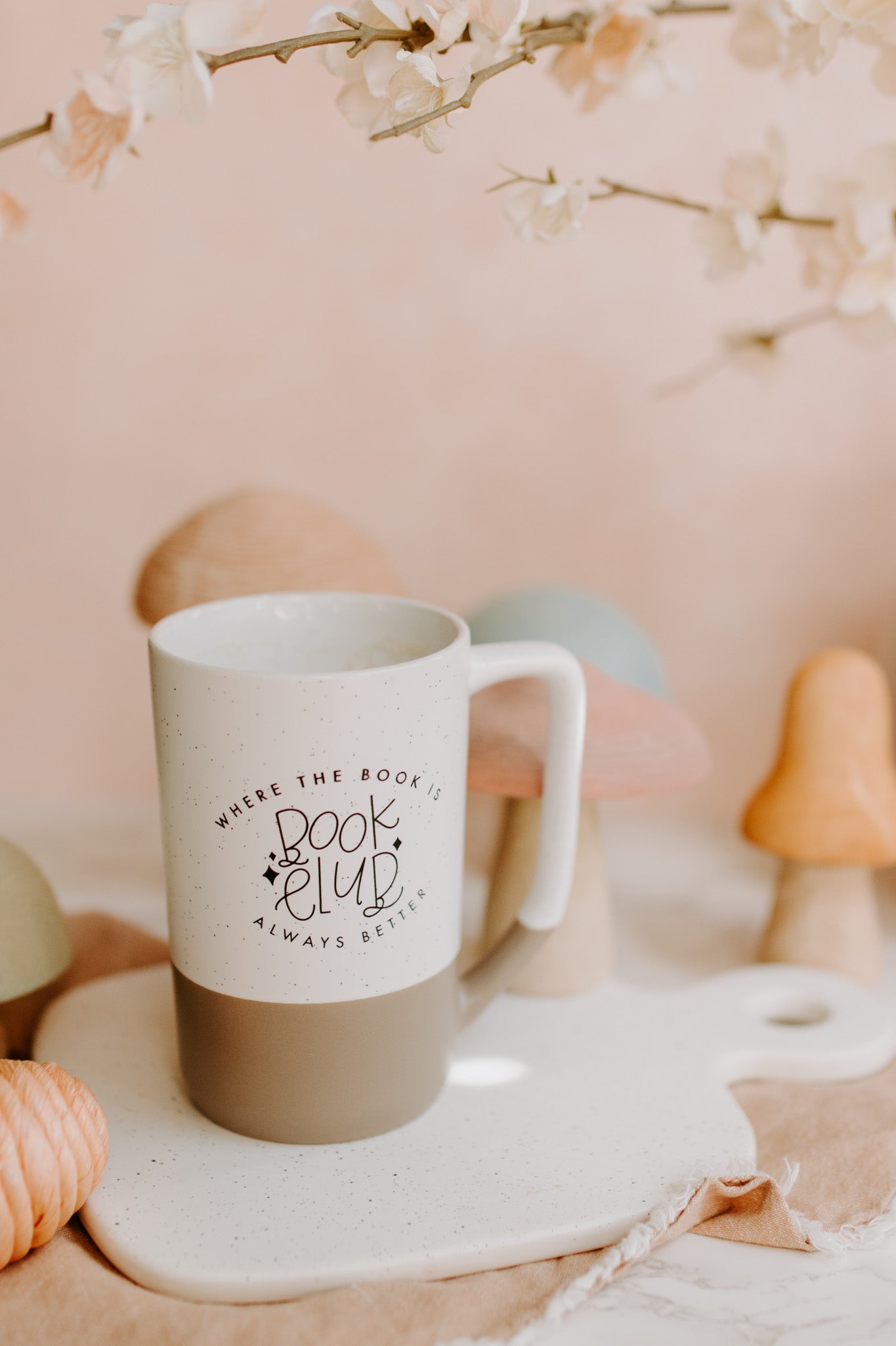 A two-tone ceramic mug with the upper part white with black speckles and the lower part taupe, featuring 'Book Club' text imprinted on the white part.