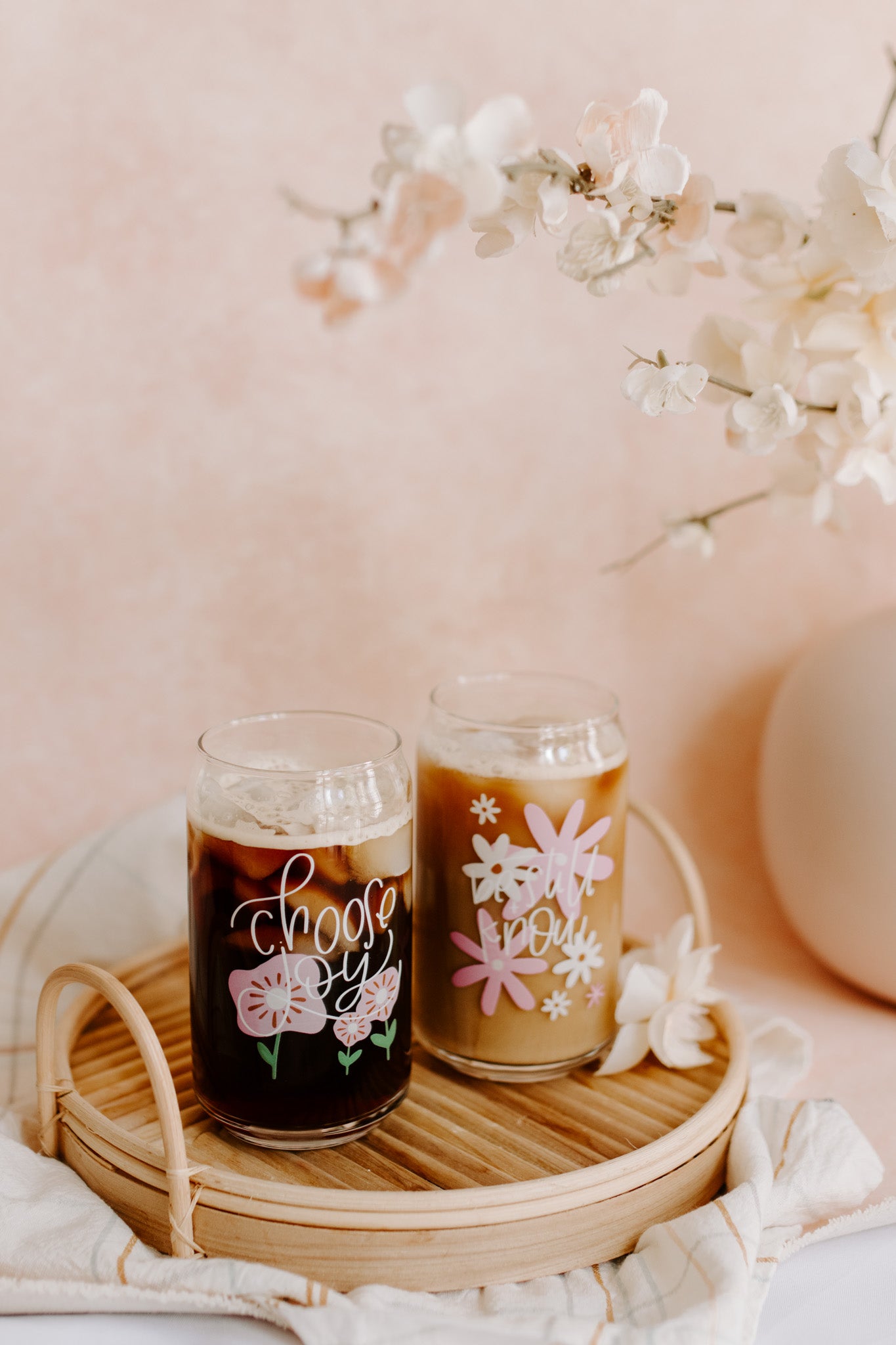 A pair of clear can-shaped glasses. One with 'choose joy' design and the other one with 'be still and know' design.