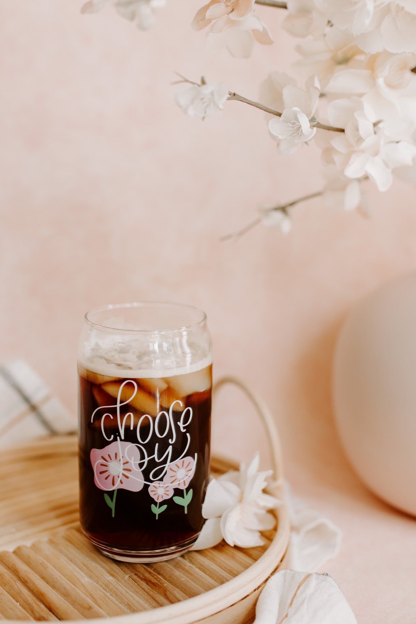 A clear can-shaped glass with 'choose joy' and floral design printed on it.