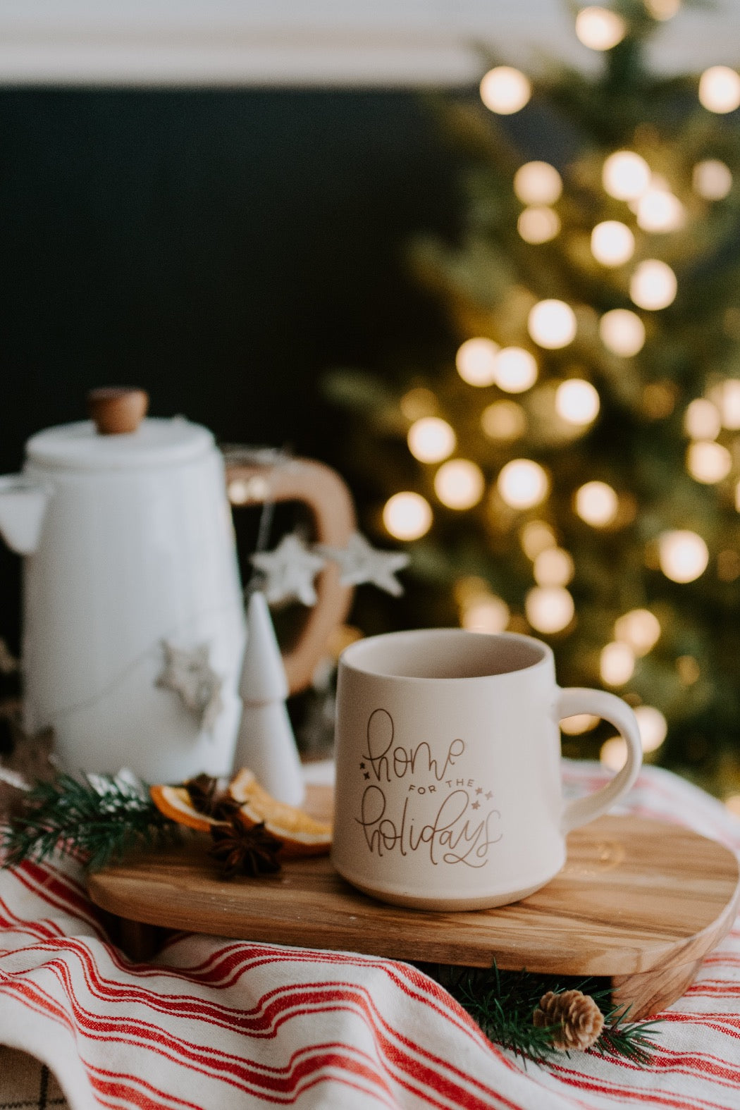 Matte beige mug with 'home for the holidays' hand lettered font printed in bronze