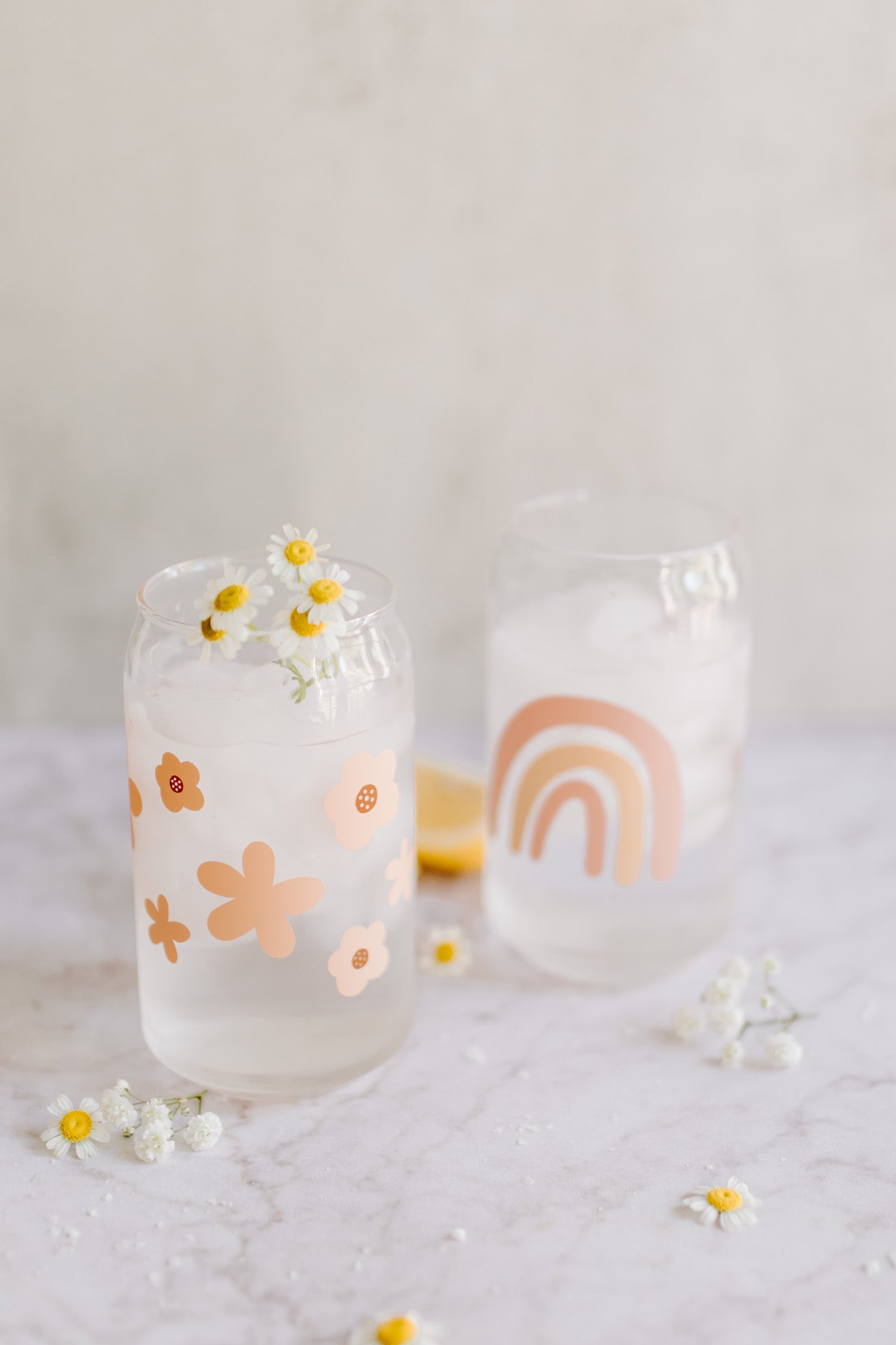 A clear can-shaped glass with a design of peach colored flowers wrapped around.