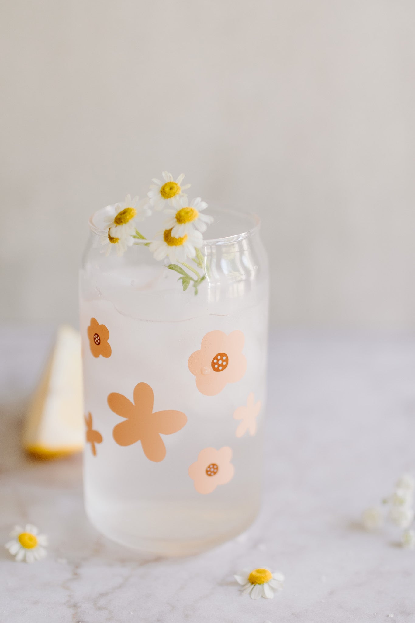 A clear can-shaped glass with a design of peach colored flowers wrapped around.