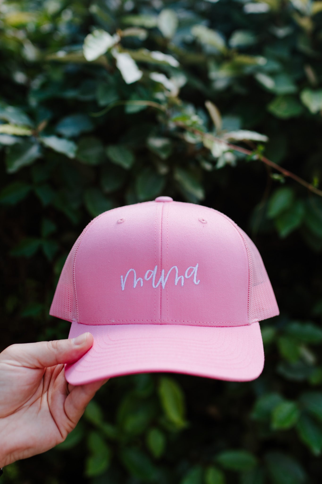 A pink embroidered retro trucker hat with the word 'Mama' stitched in white thread on the front.