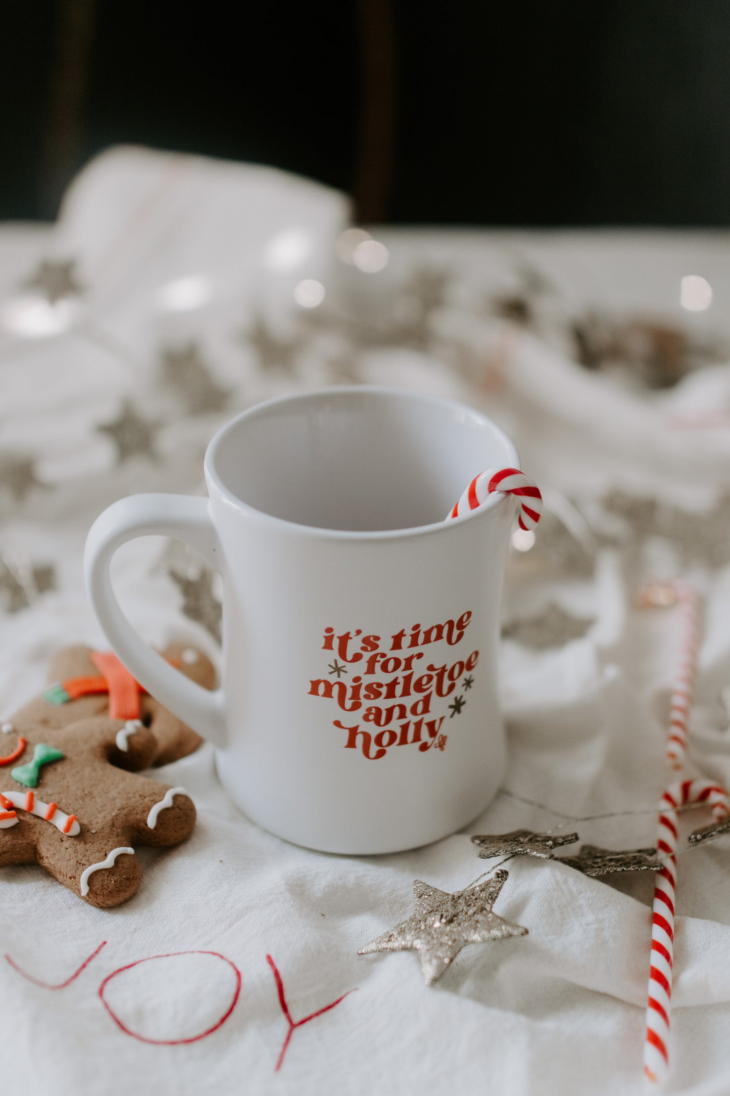 A matte white ceramic mug with 'its time for mistletoe and holly' printed in vintage red and gold.