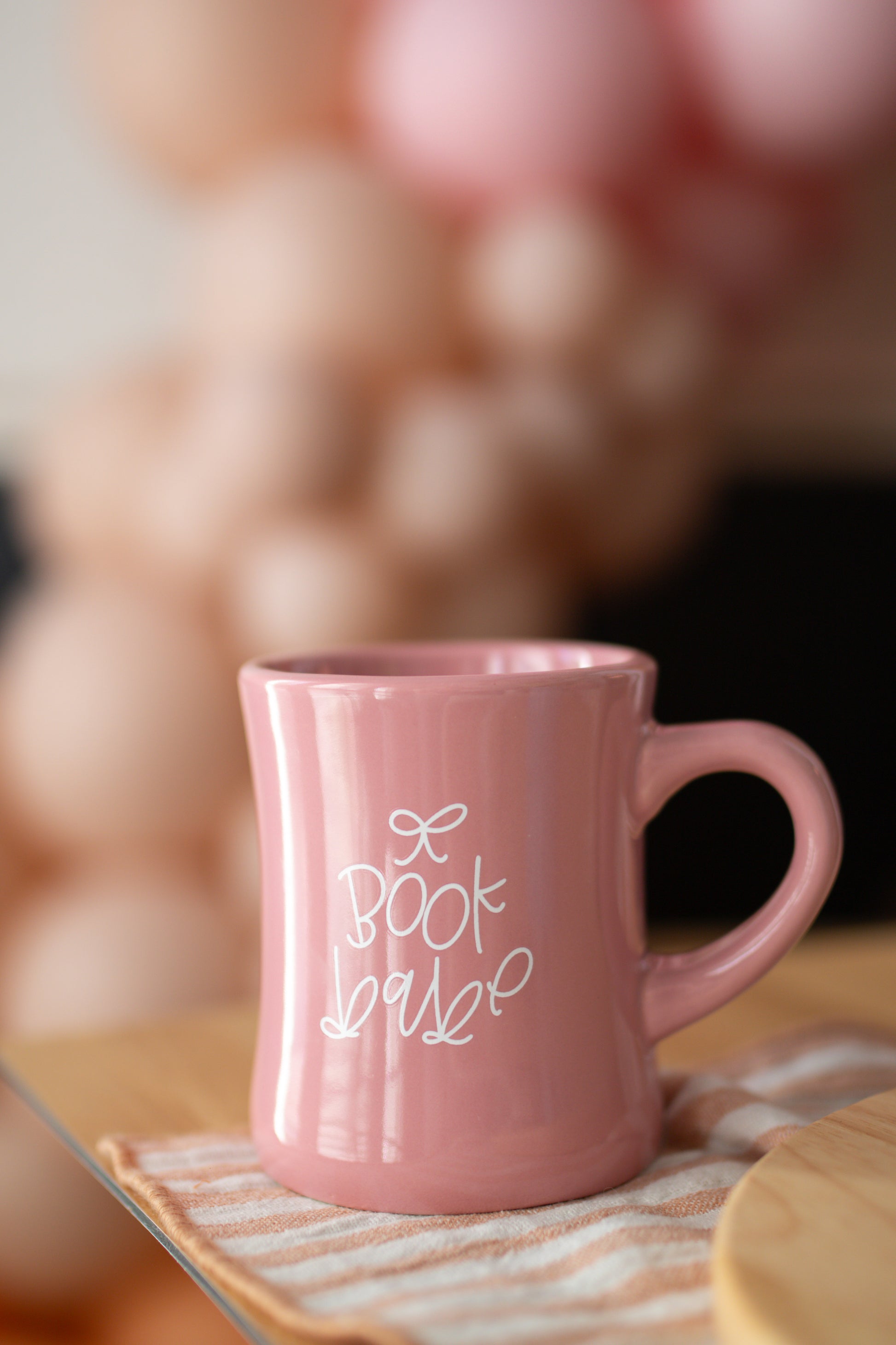 A glossy pink ceramic mug with 'book babe' printed in white hand-lettering and a small bow detail.