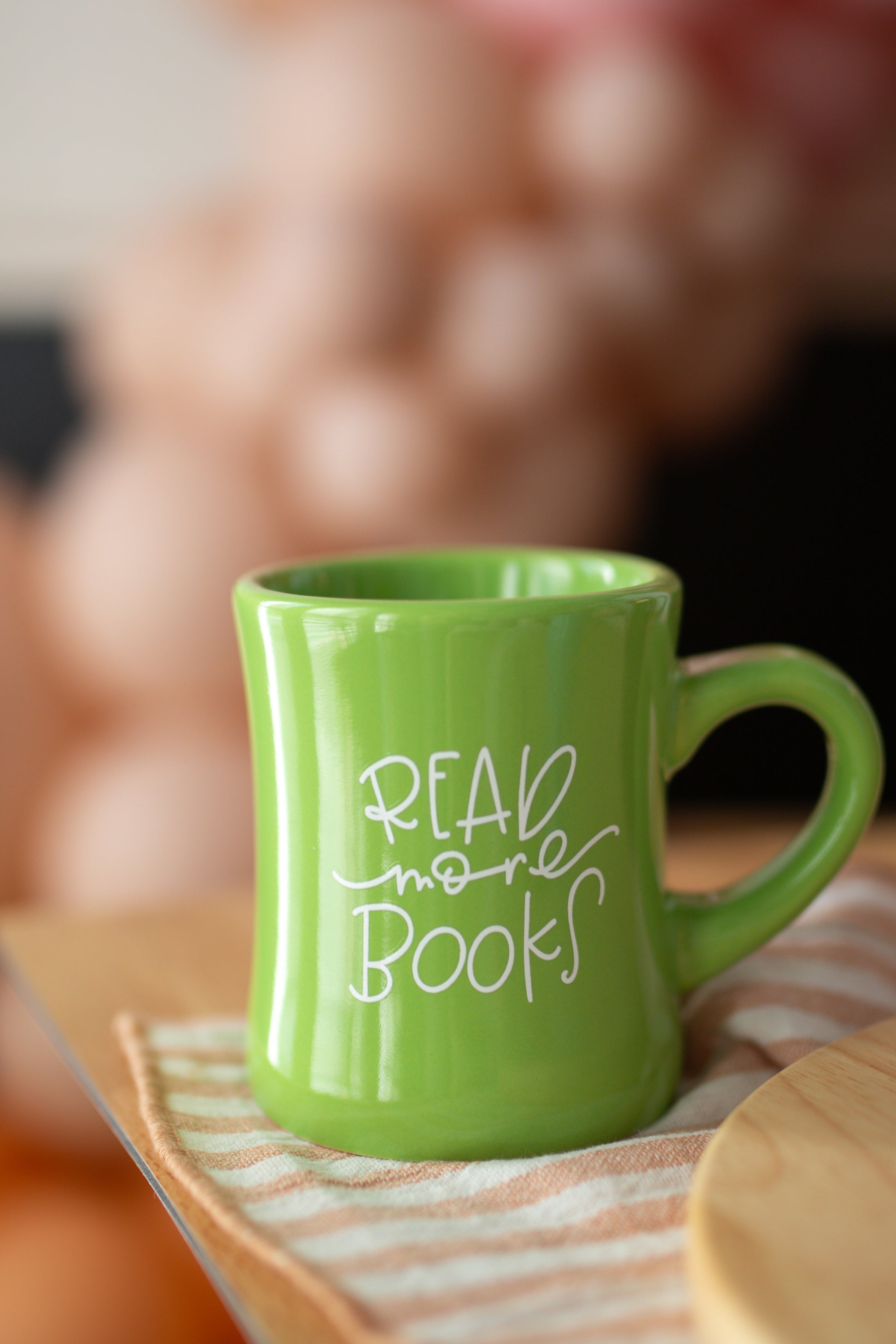 A green ceramic mug with the phrase 'READ more books' written in white hand-lettering on the side.