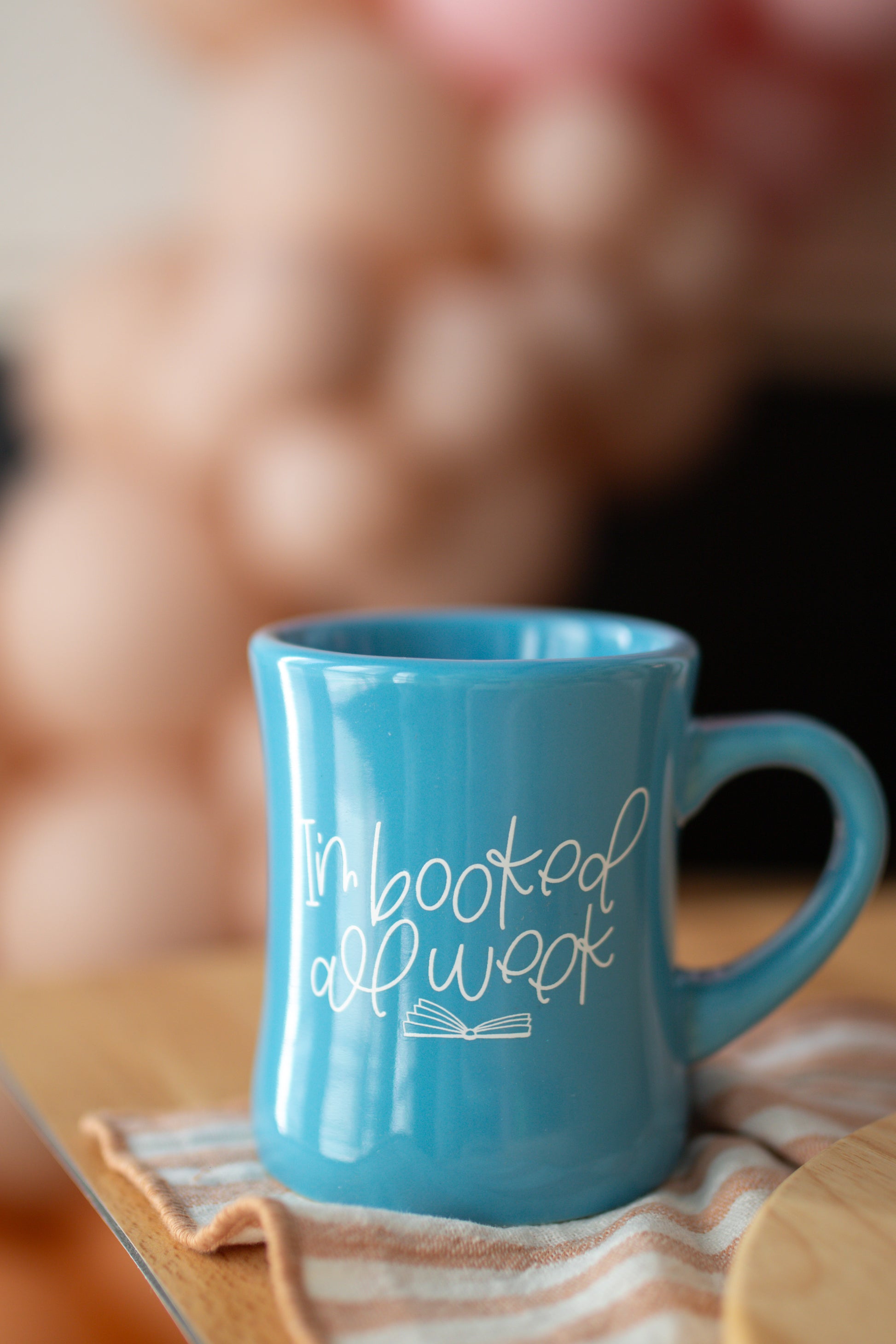 A blue ceramic mug with the text 'I'm booked all week' printed on it, featuring an open book graphic.