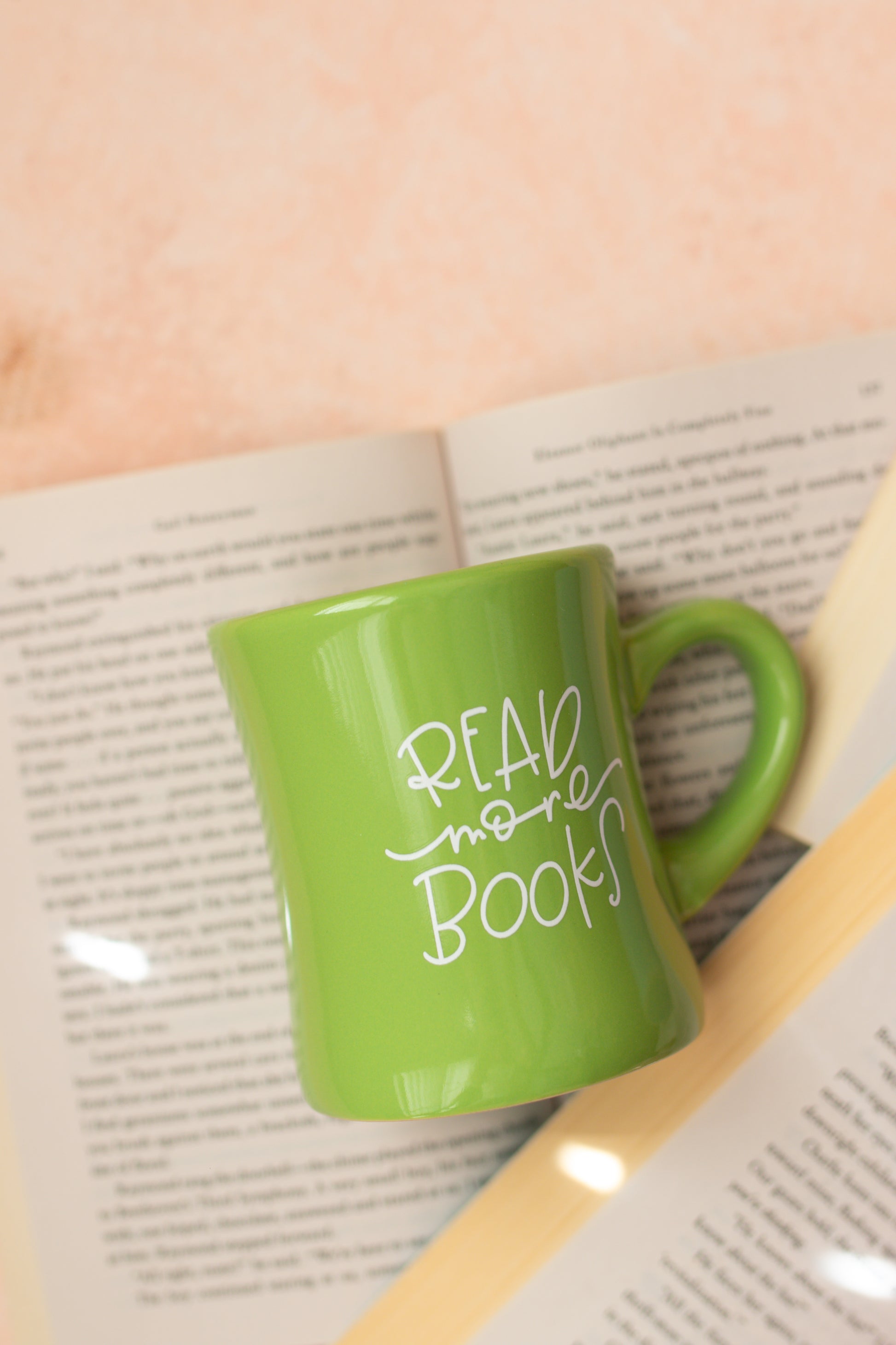 A green ceramic mug with the phrase 'READ more books' written in white hand-lettering on the side.