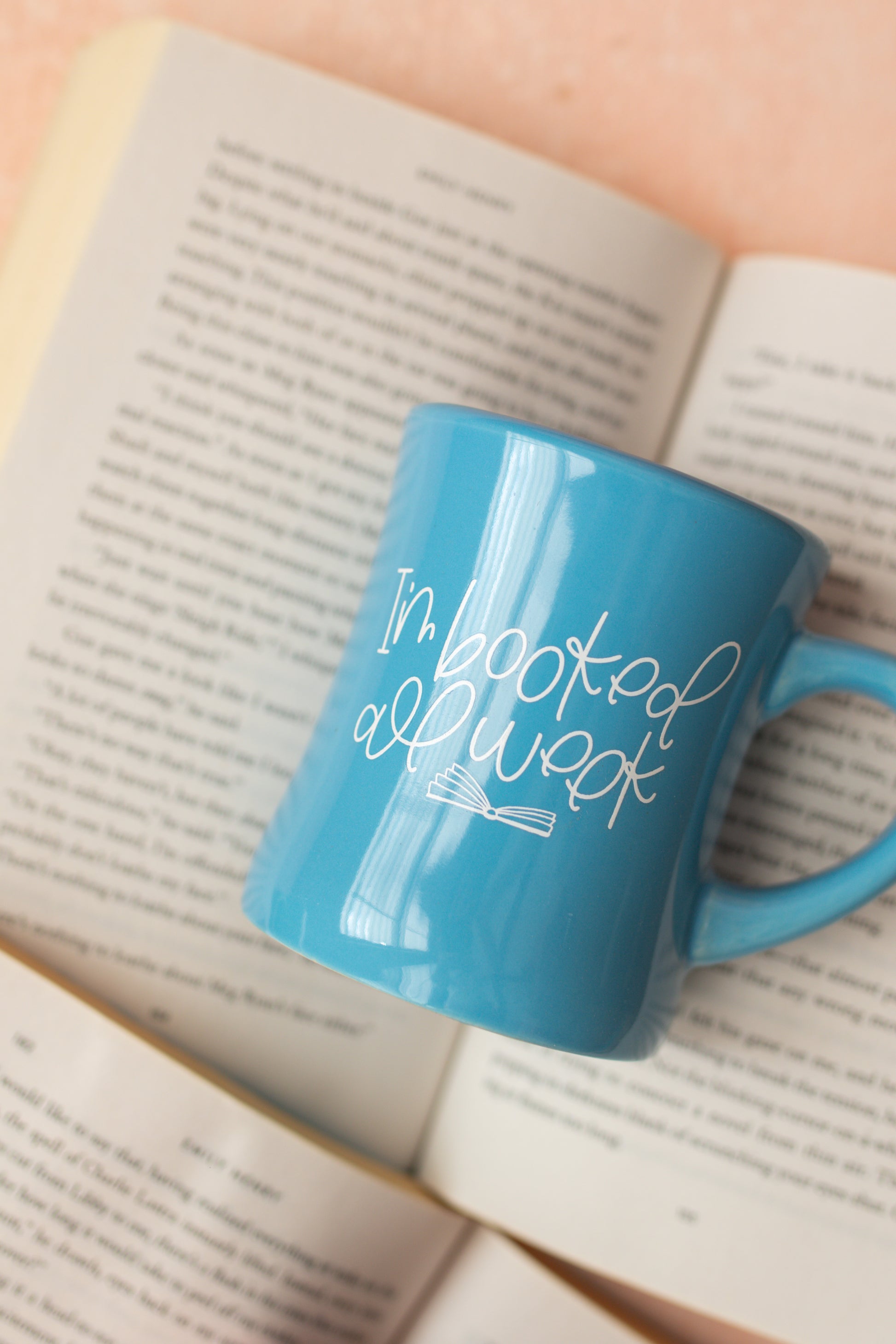 A blue ceramic mug with the text 'I'm booked all week' printed on it, featuring an open book graphic.