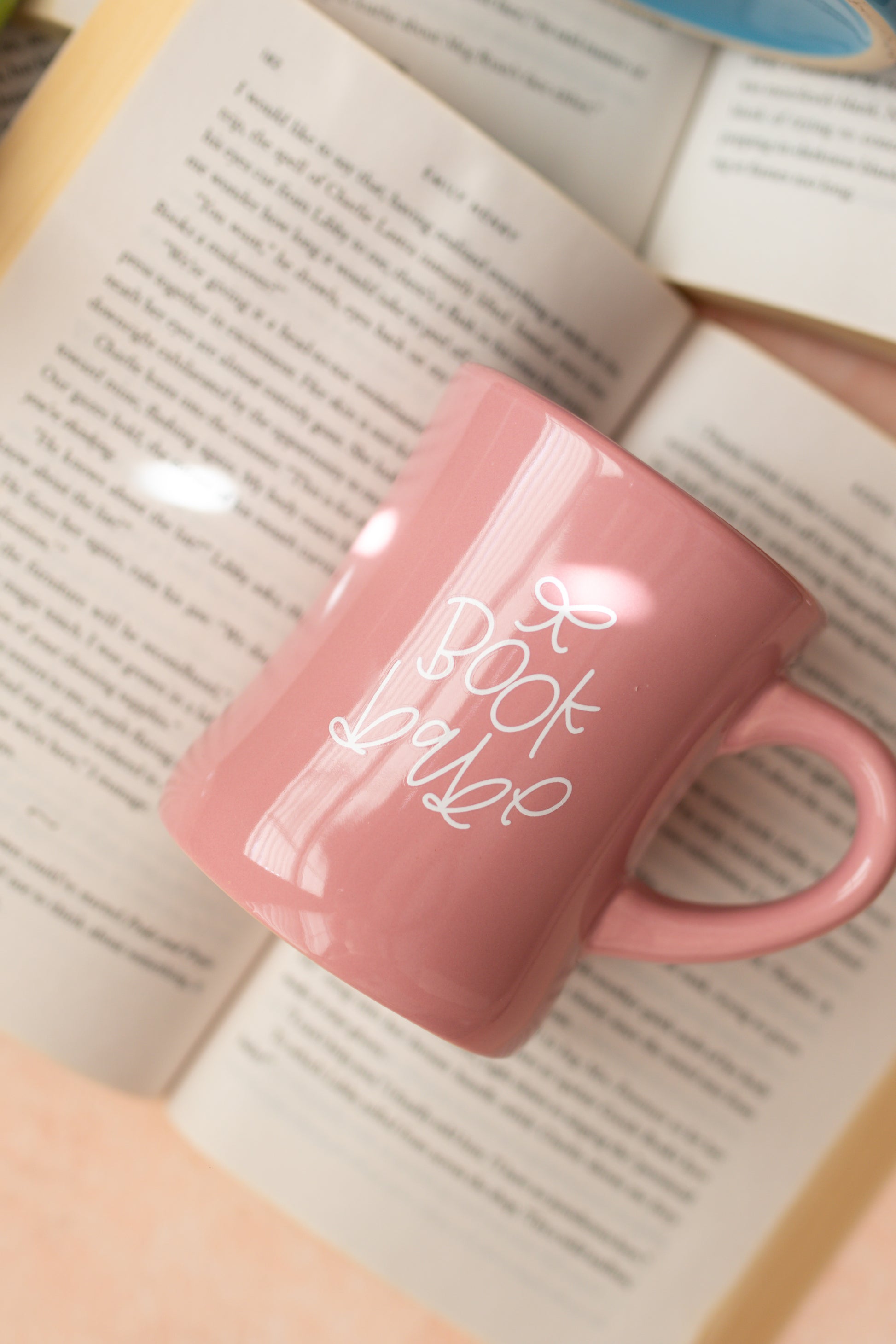 A glossy pink ceramic mug with 'book babe' printed in white hand-lettering and a small bow detail.