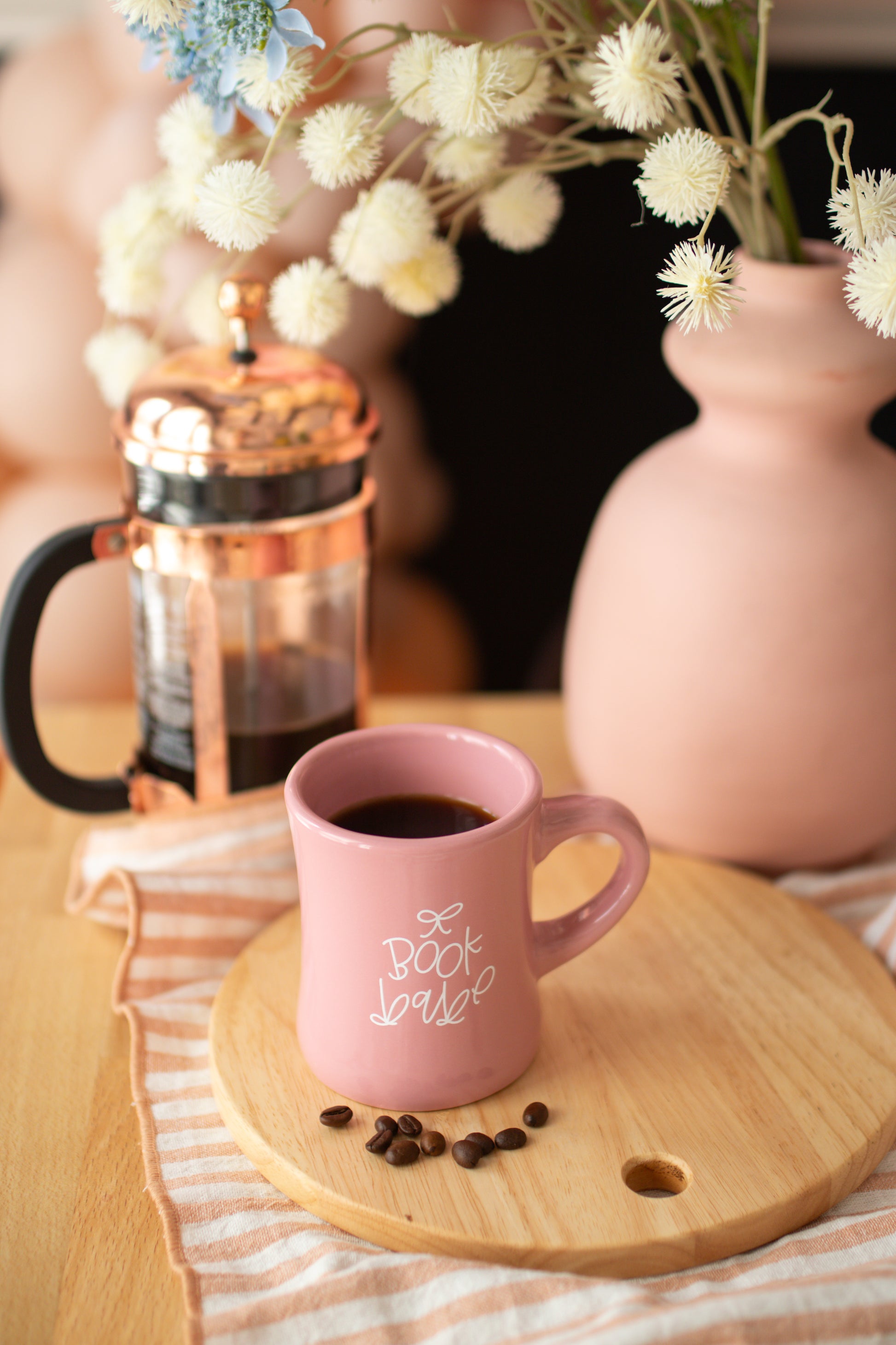 A glossy pink ceramic mug with 'book babe' printed in white hand-lettering and a small bow detail.