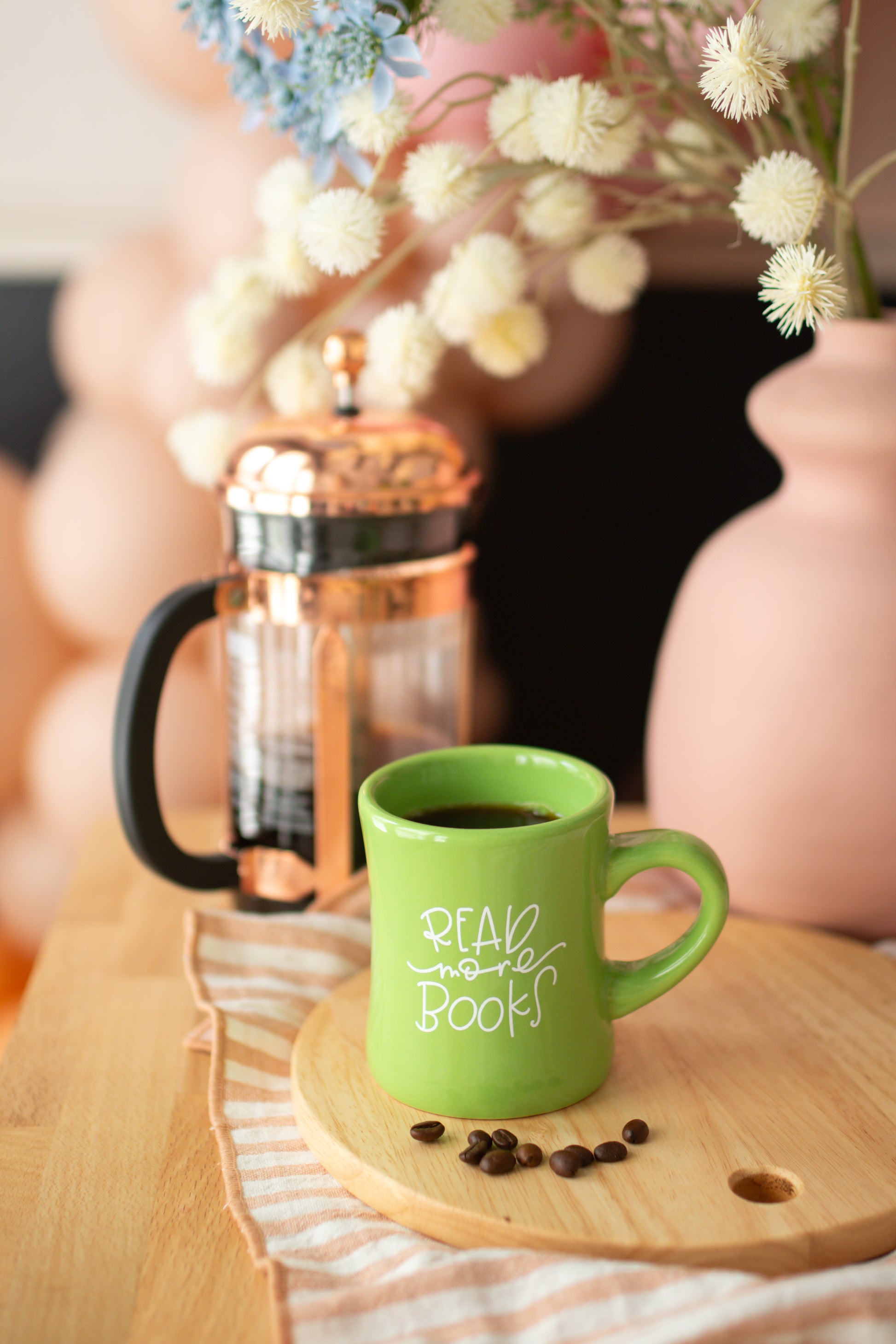 A green ceramic mug with the phrase 'READ more books' written in white hand-lettering on the side.