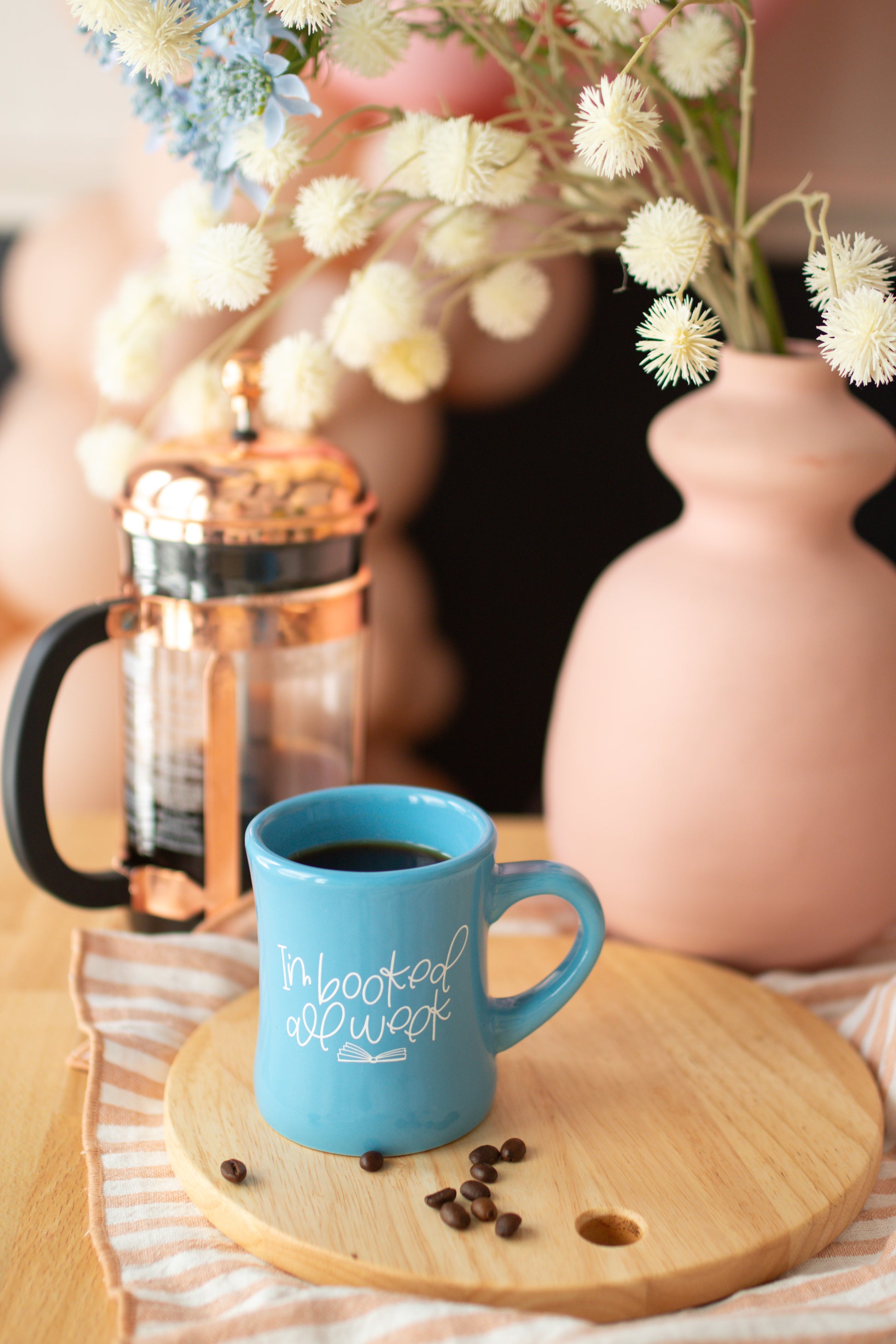 A blue ceramic mug with the text 'I'm booked all week' printed on it, featuring an open book graphic.