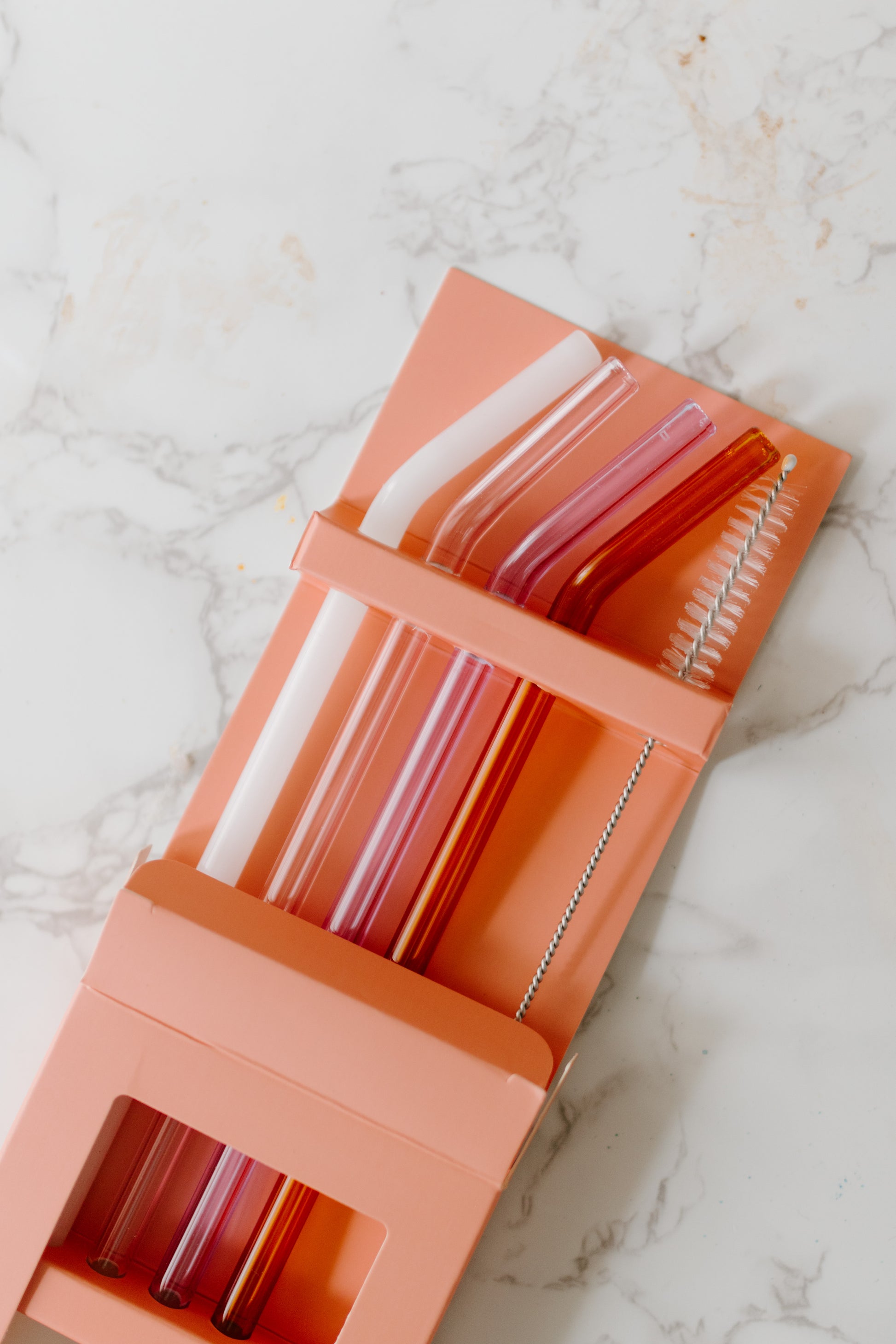 A set of four multicolored glass straws in Milky White, Lilac, Pink, and Amber colors with straw brush cleaner included