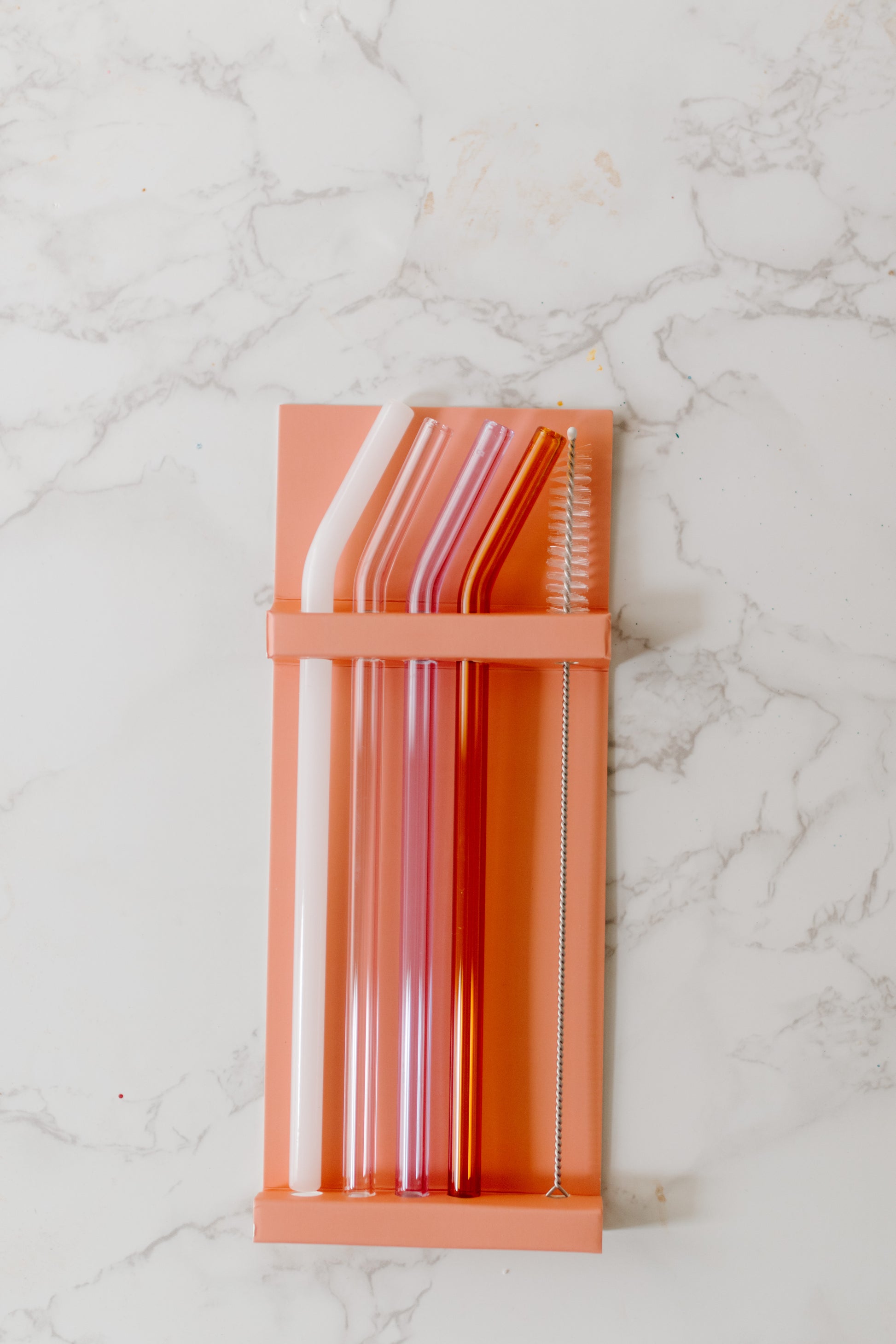 A set of four multicolored glass straws in Milky White, Lilac, Pink, and Amber colors with straw brush cleaner included