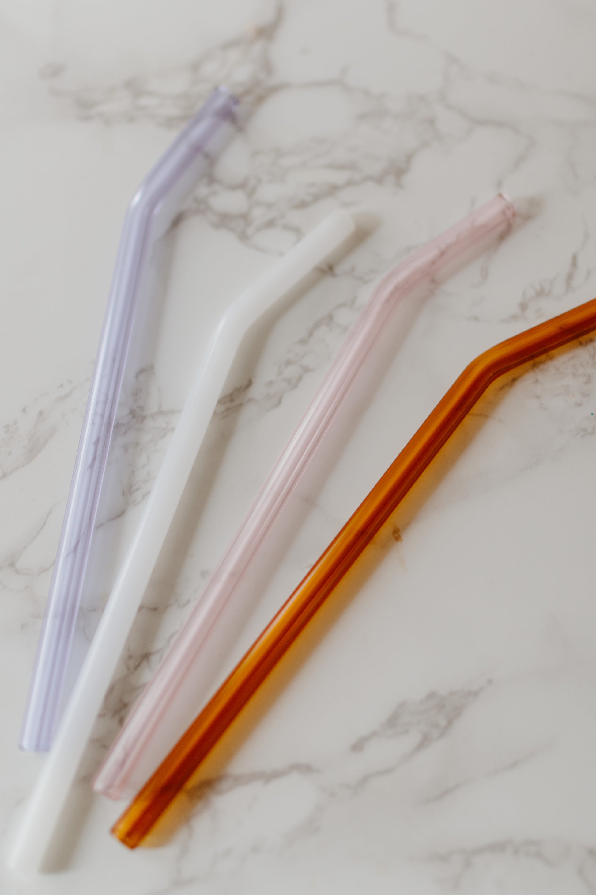 A set of four multicolored glass straws in Milky White, Lilac, Pink, and Amber colors