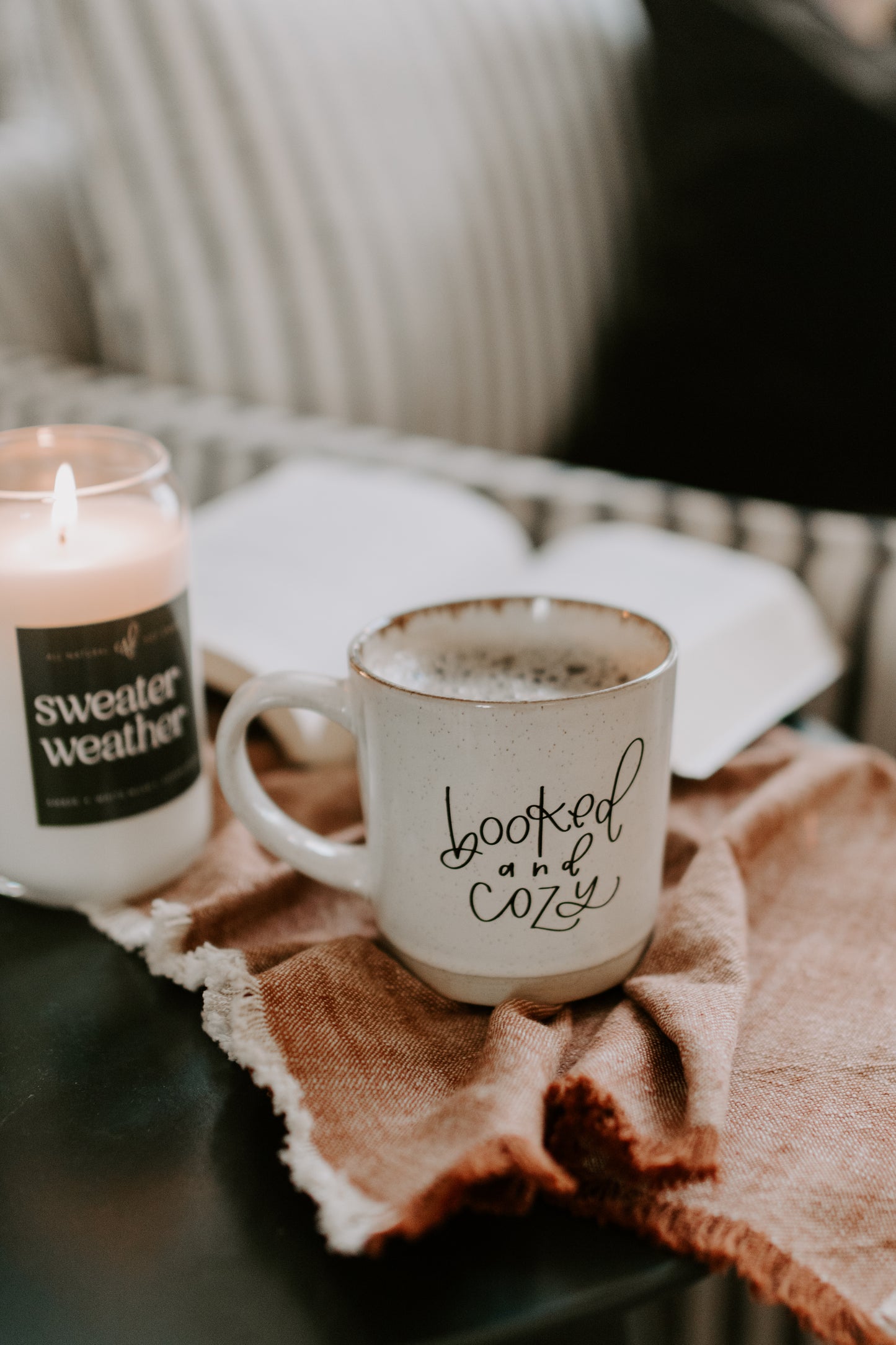 Cup with 'loved and cozy' text and candle on a table with a blanket