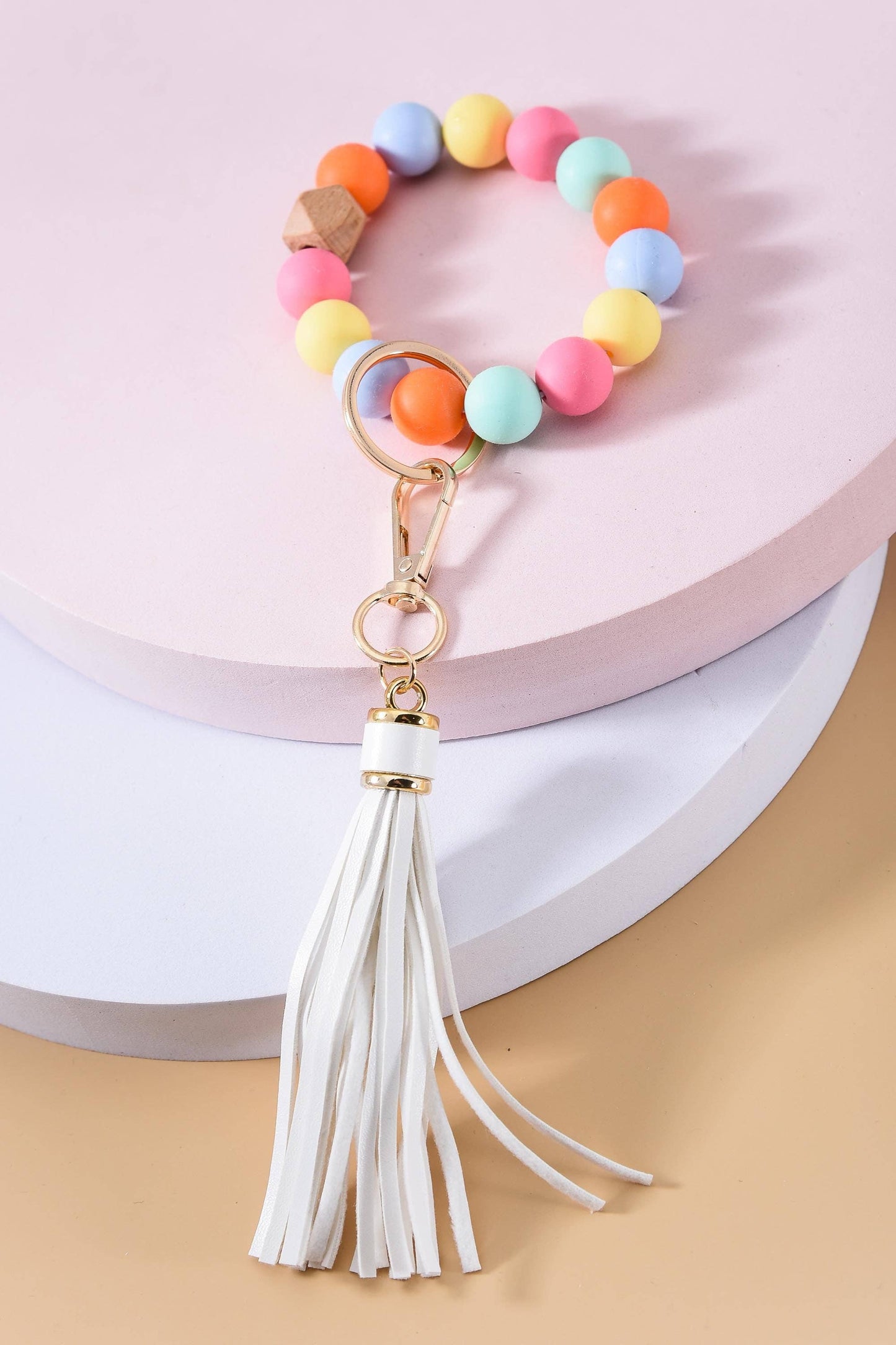A multicolored rubber bead key holder with a white suede tassel and gold plating on the metal clasp, displayed against a neutral background.