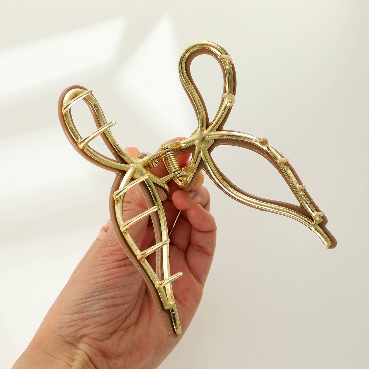 A large ribbon bow metal claw clip in a color variation of gold and beige, designed for holding medium to thick hair.