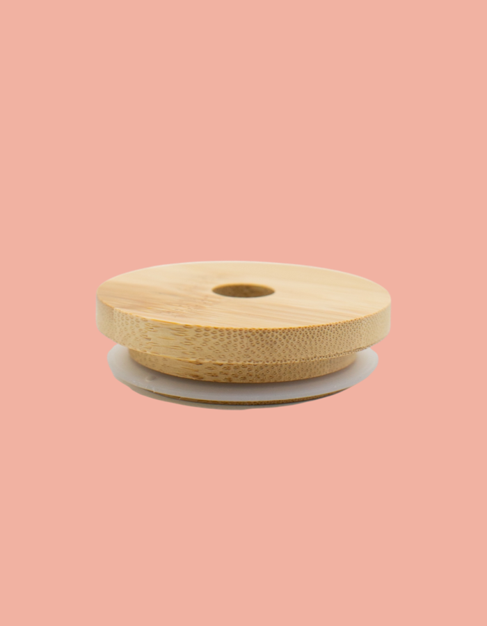 A beige bamboo glass lid with a central straw hole, displayed on a pink background.