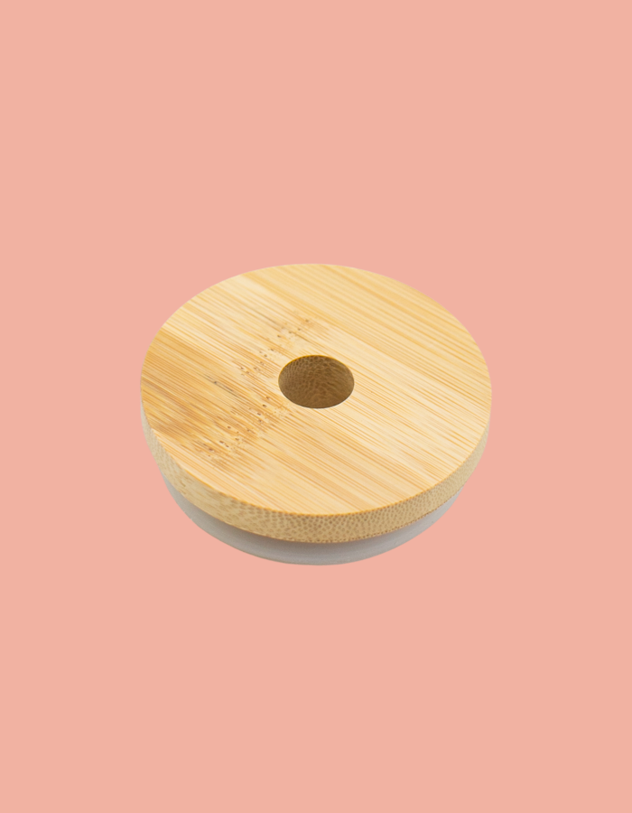 A beige bamboo glass lid with a central straw hole, displayed on a pink background.
