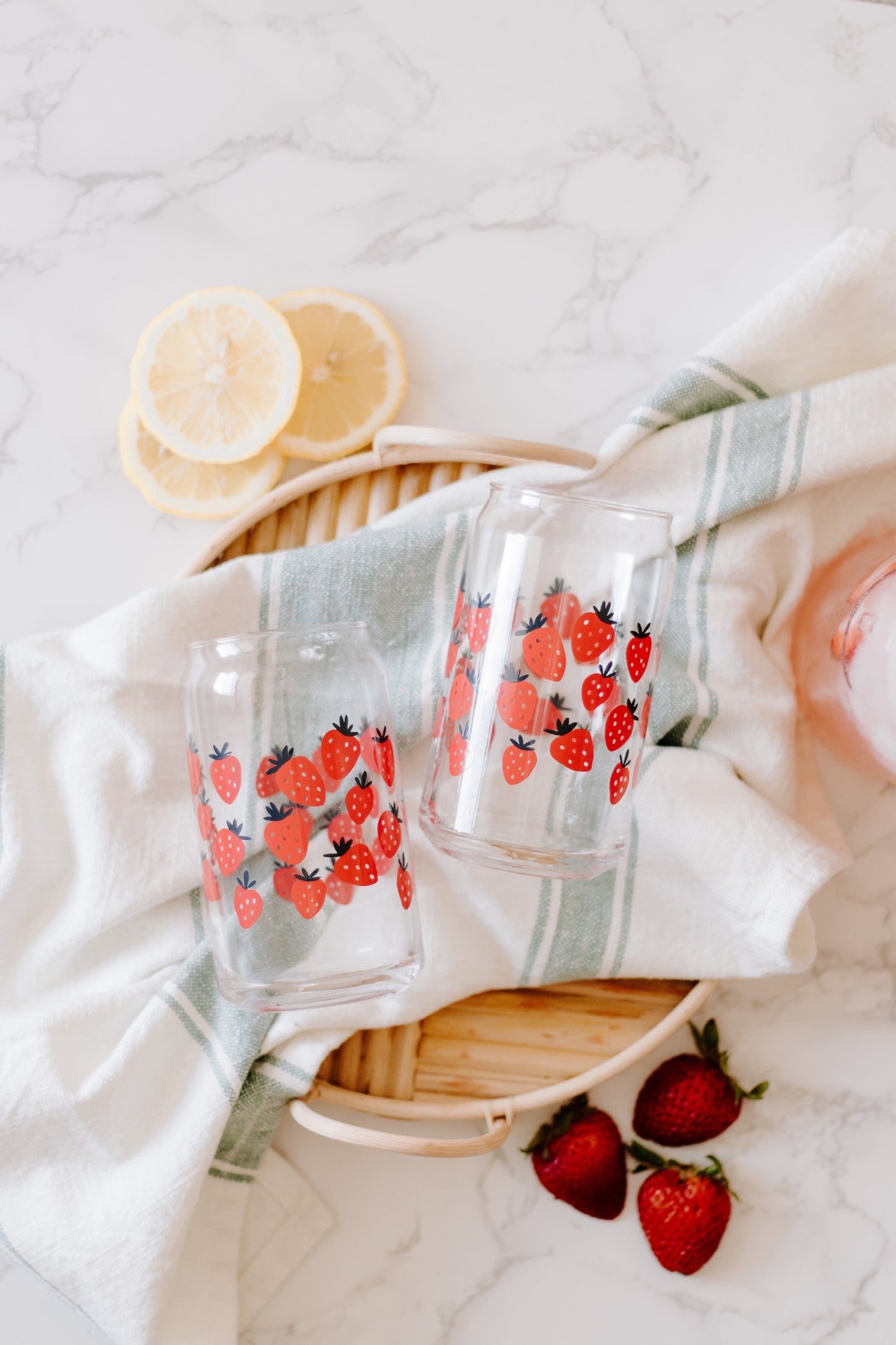 A clear can-shaped glass with strawberry design wrapped around.