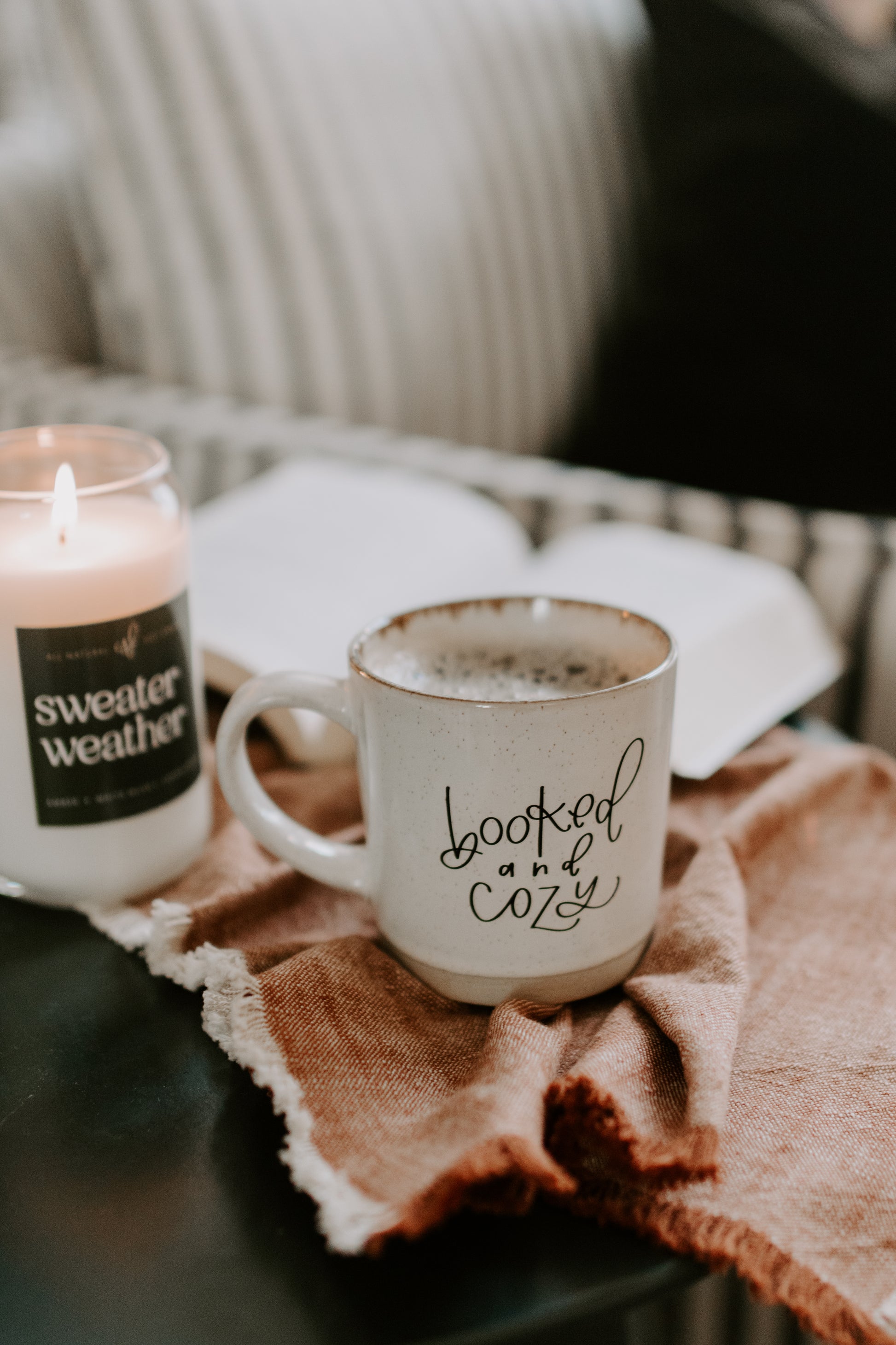 Cup with 'loved and cozy' text and candle on a table with a blanket