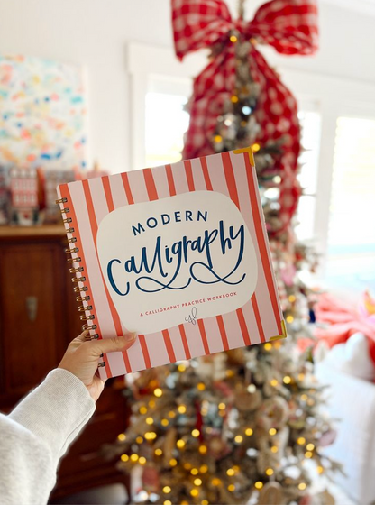 Person holding a 'Modern Calligraphy' book with a decorated Christmas tree in the background
