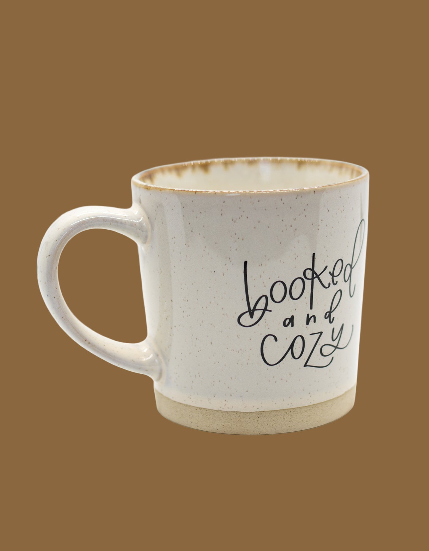 White ceramic mug with 'booked and cozy' text on a brown background