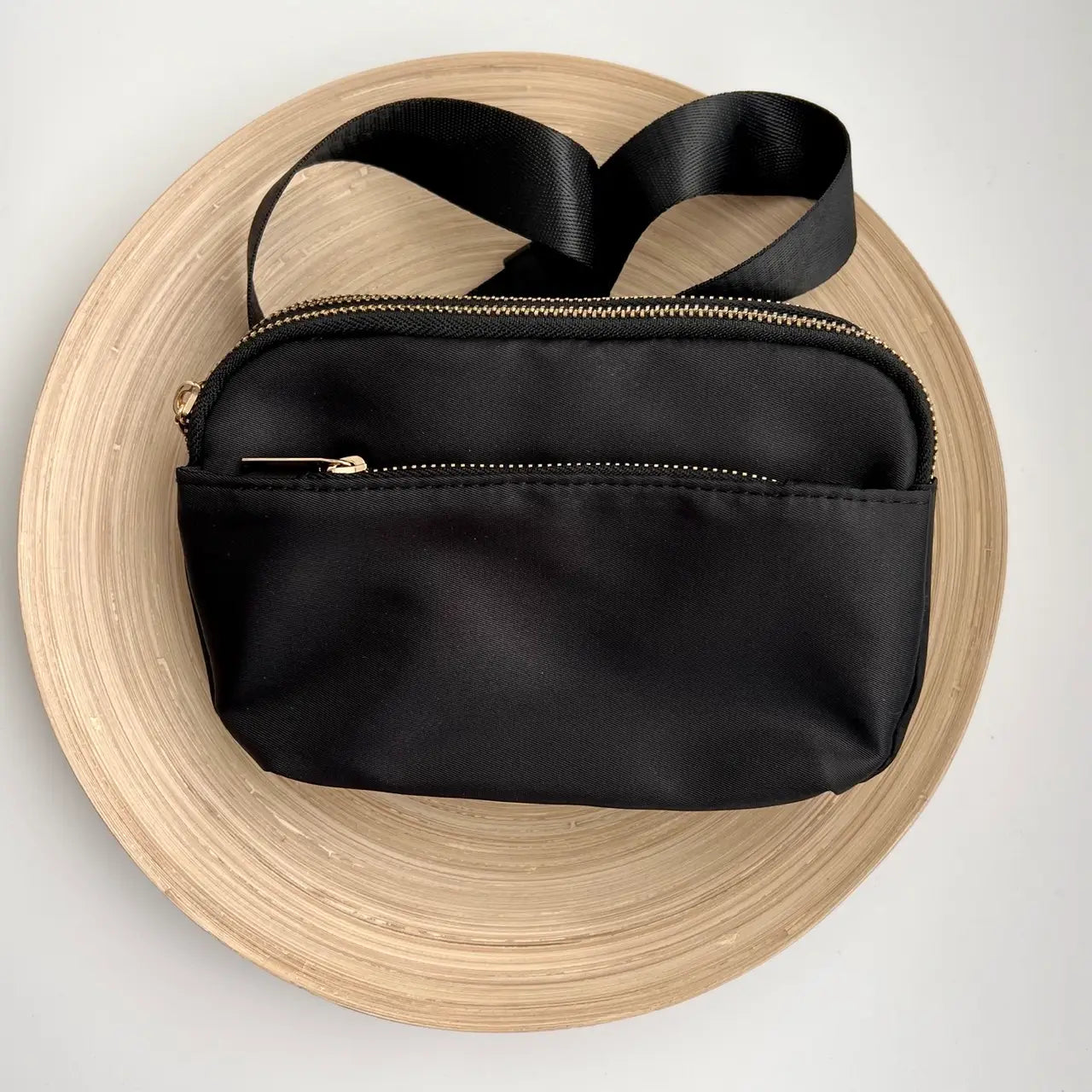 A black crossbody belt bag with a buckle strap and multiple zippered pockets.