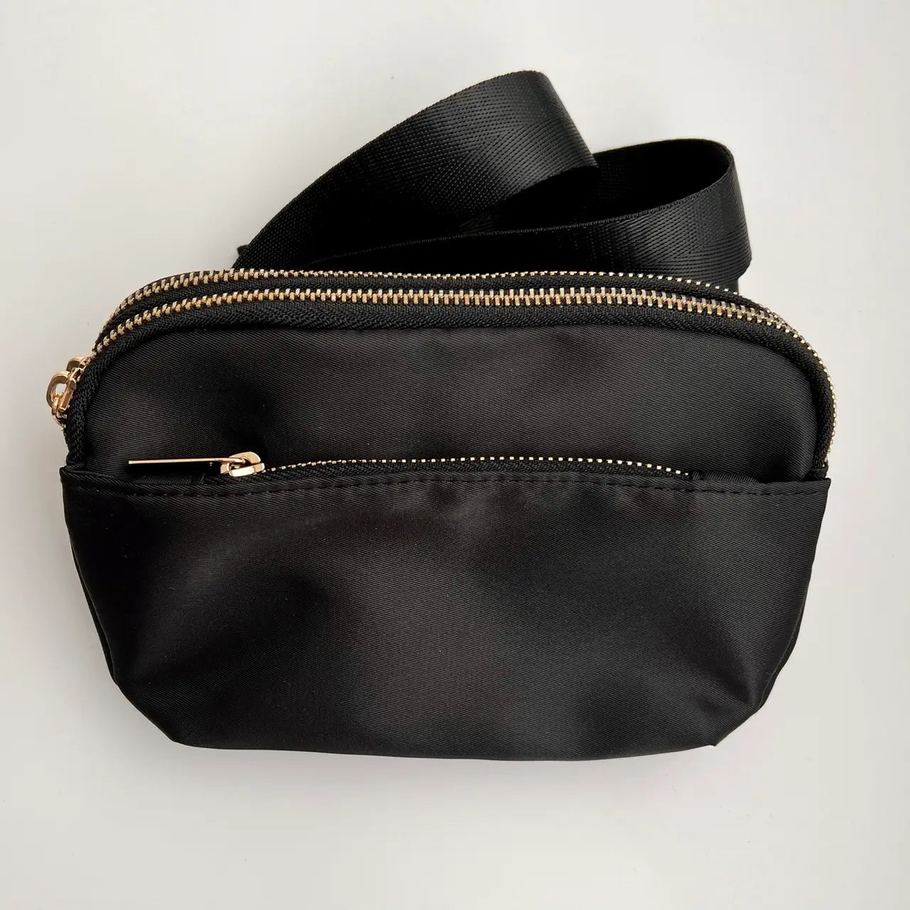 A black crossbody belt bag with a buckle strap and multiple zippered pockets.