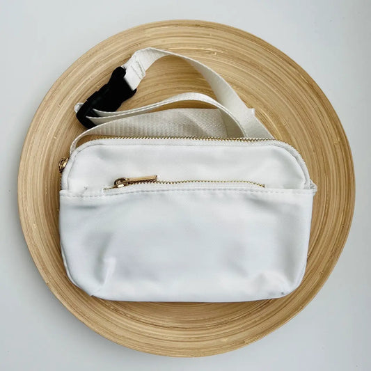 A white crossbody belt bag with a buckle strap and multiple zippered pockets.
